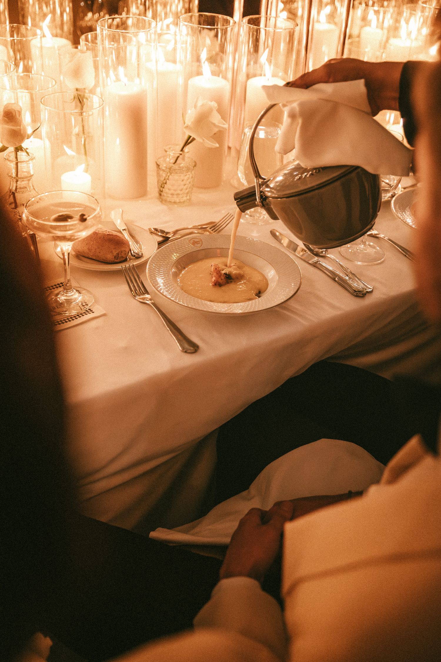 Server pouring soup into a bowl at an elegant candlelit wedding dinner table setting.