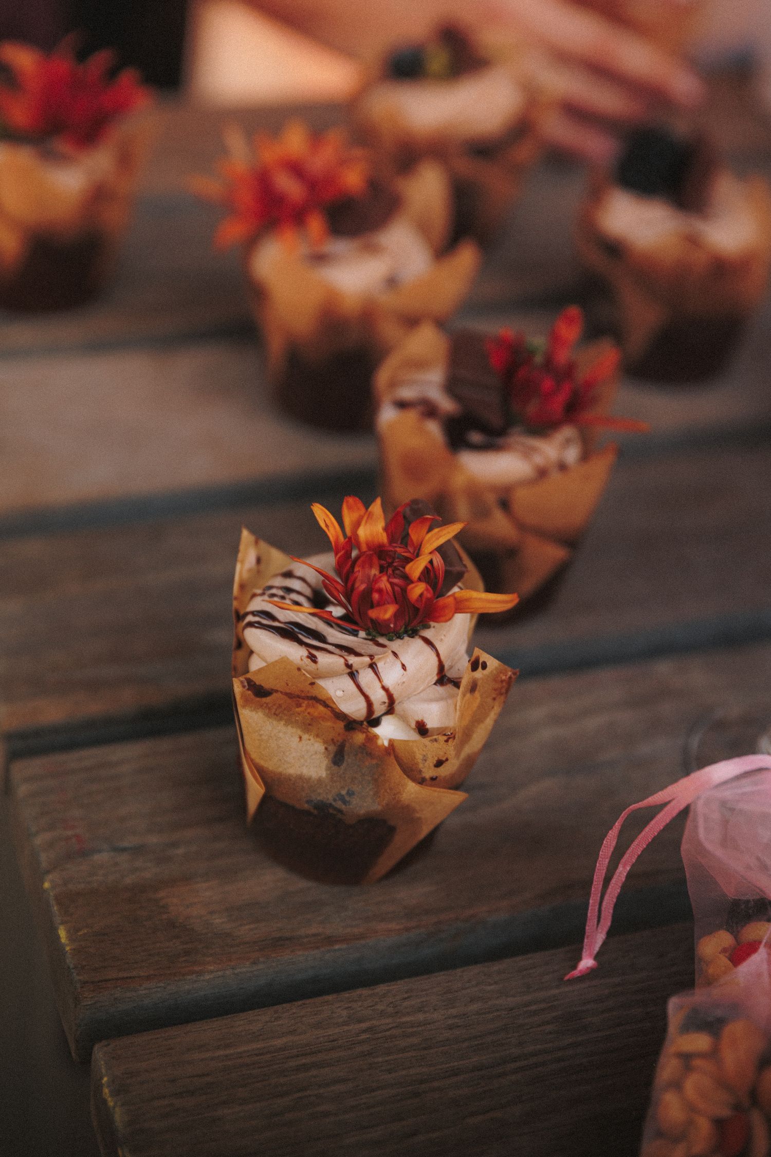 Decorative mini dessert cups topped with chocolate drizzle and red floral garnishes displayed on a rustic wooden surface.