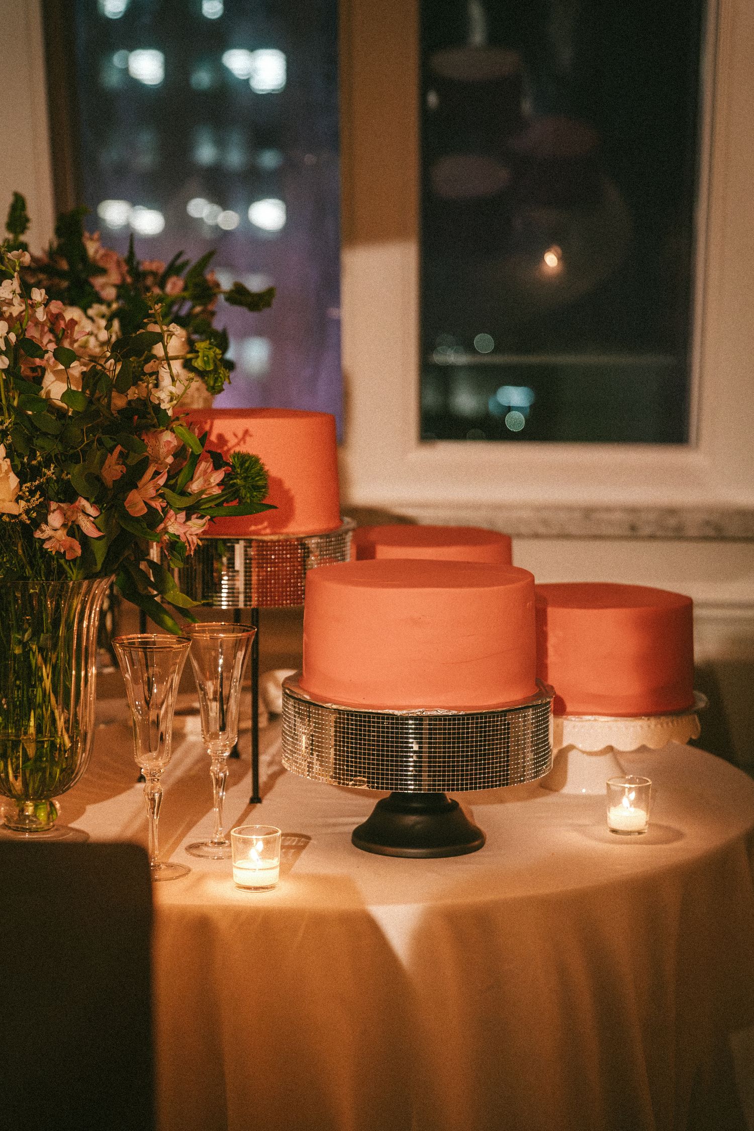 Elegant wedding cake display with coral-colored tiered cakes on stands beside fresh floral arrangements.