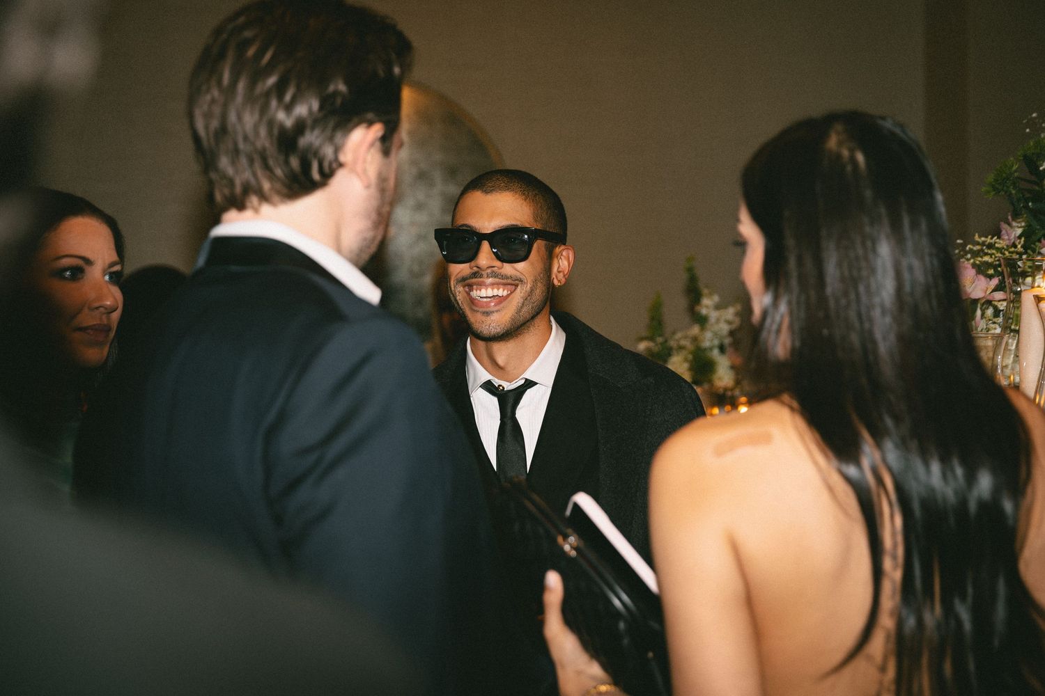 A smiling guest in sunglasses and black suit mingles at an elegant wedding reception.