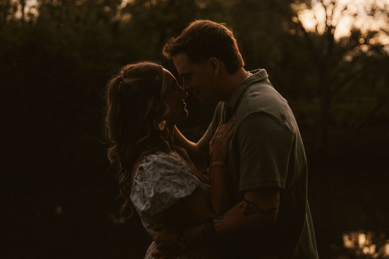 Romantic couple sharing a kiss silhouetted against a warm golden sunset outdoors.