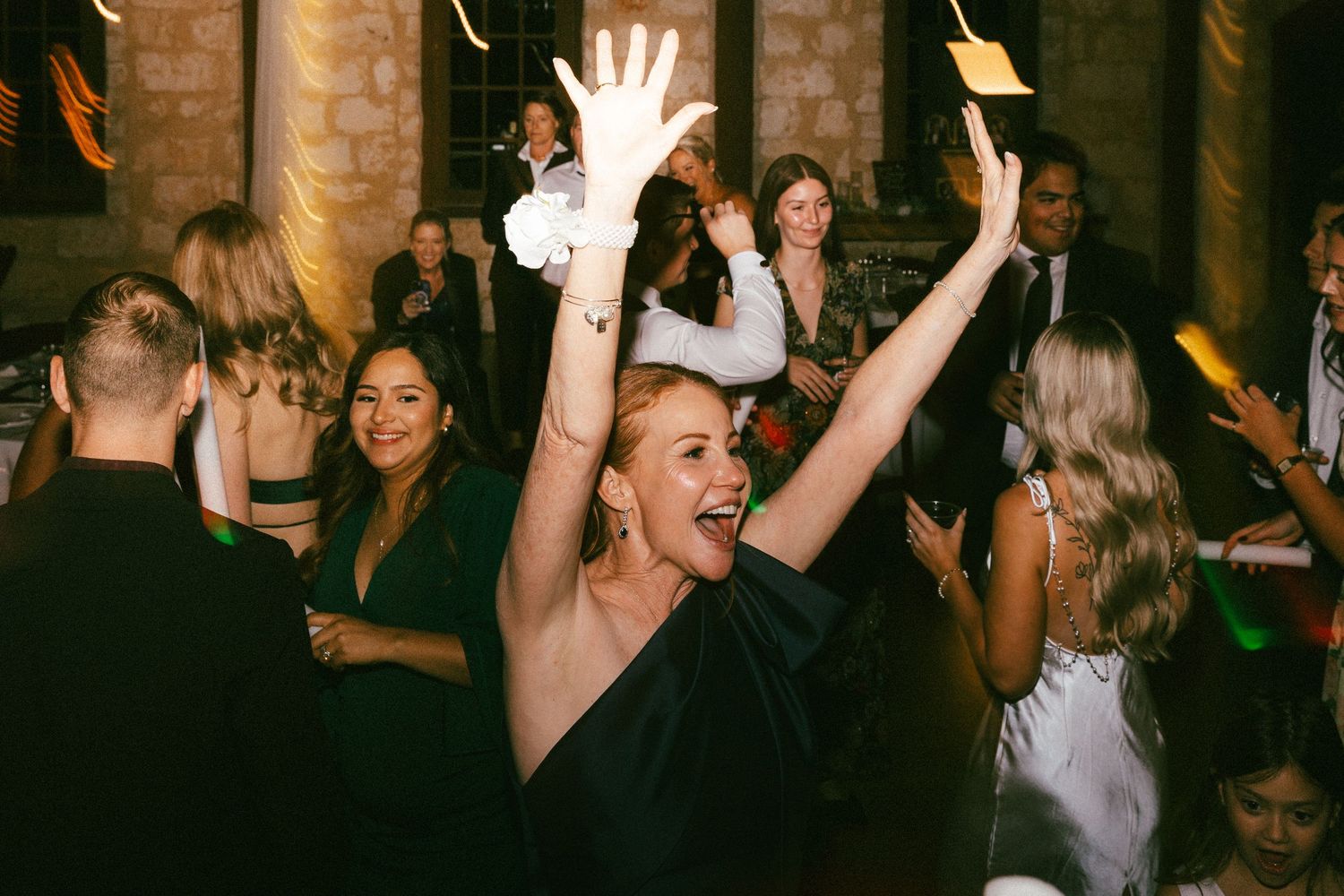 Excited wedding guest dancing with arms raised at lively indoor wedding reception party.