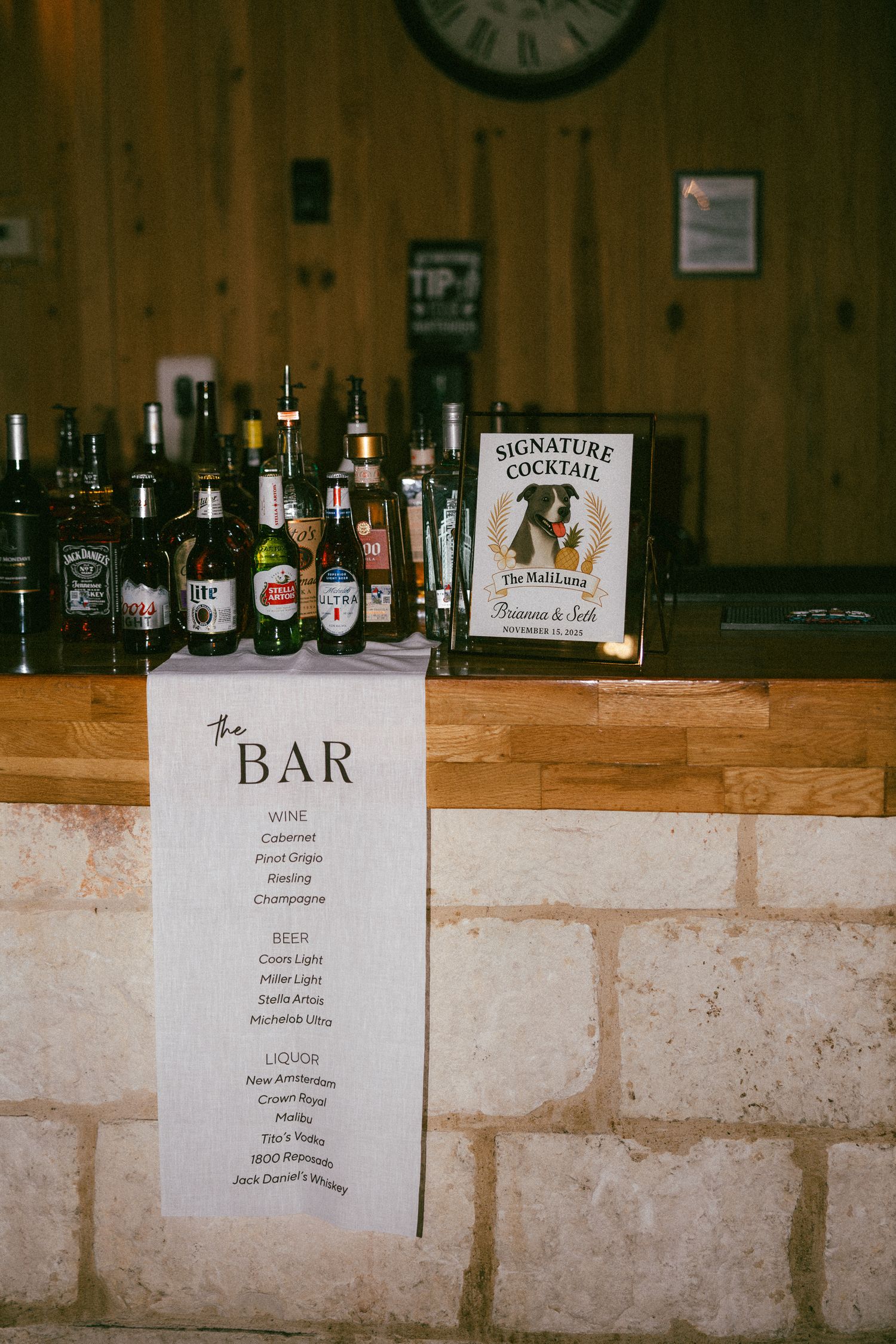 Rustic wedding bar display with signature cocktail sign, wine, beer, and liquor bottle selections.