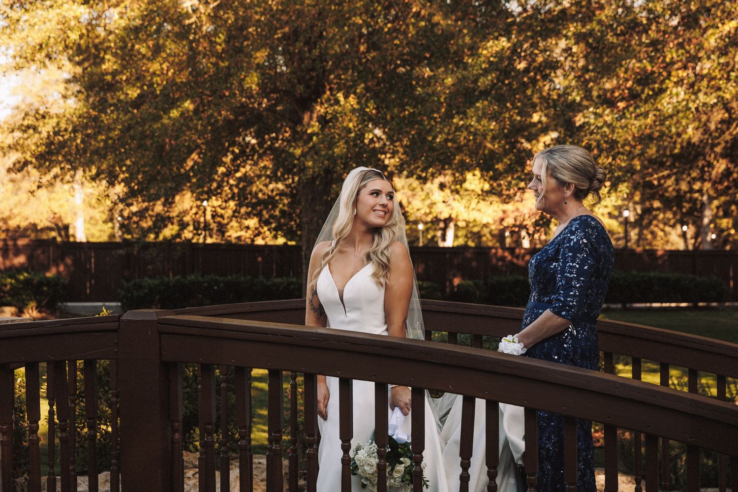 Bride in white gown and veil sharing a joyful moment on a wooden deck at golden hour.