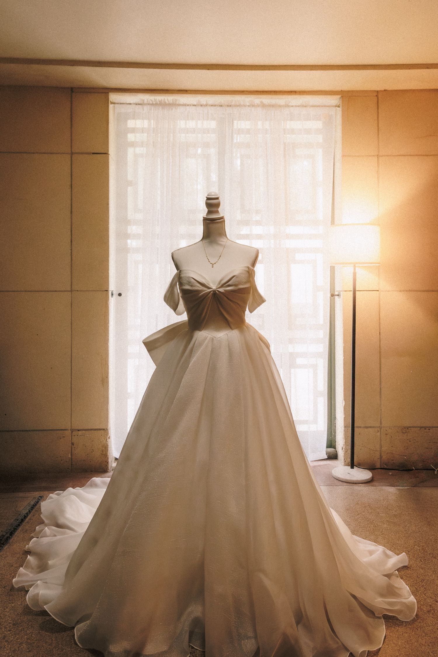 Elegant off-shoulder white ballgown wedding dress displayed on a mannequin in a warmly lit bridal suite.