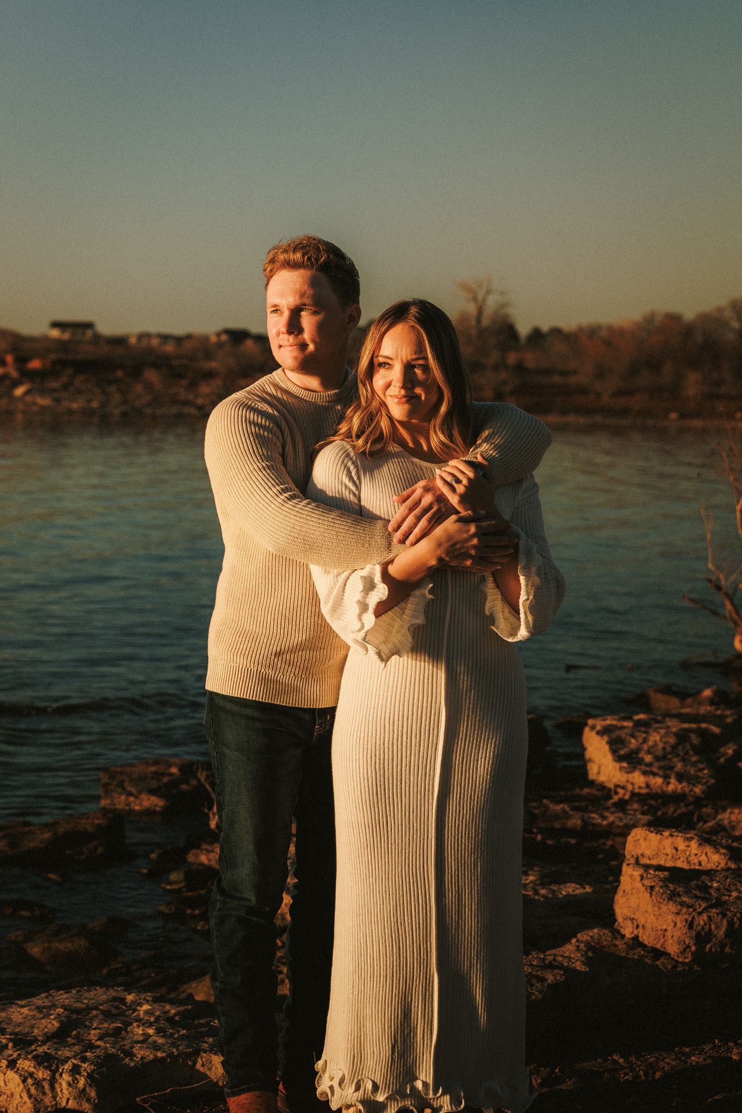 A romantic sunset photoshoot by the water with a couple embracing on rocky terrain.