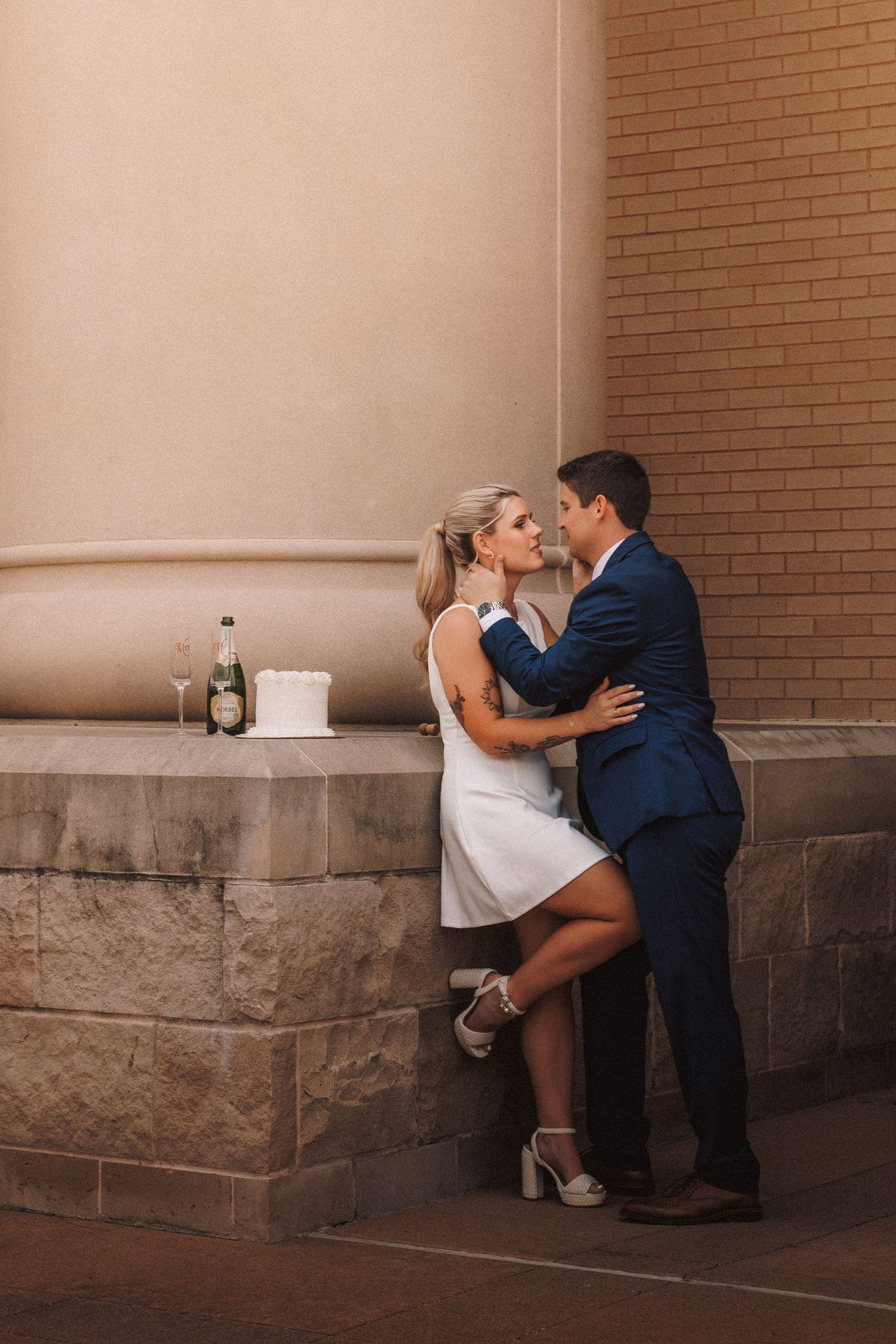 Romantic sequence of wedding couple embracing against brick and stone wall with columns.