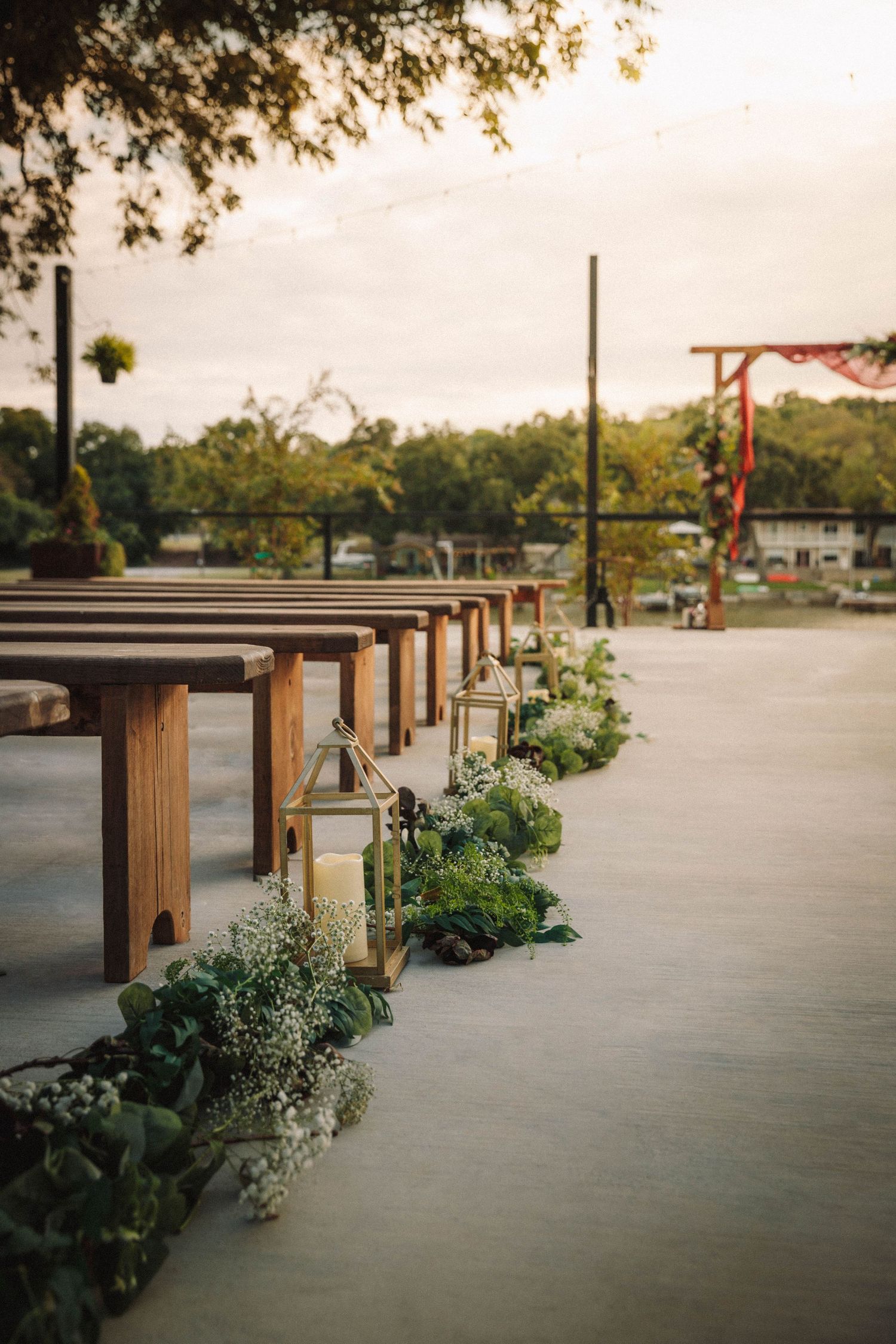 Wooden benches and planters line a concrete pathway in an outdoor space at sunset.