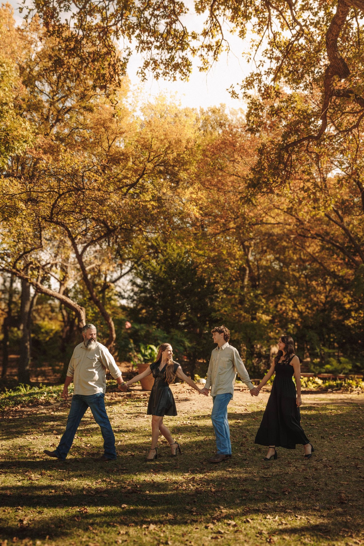 Multiple people play and pose on an autumn hillside in a park setting during golden hour sunlight.