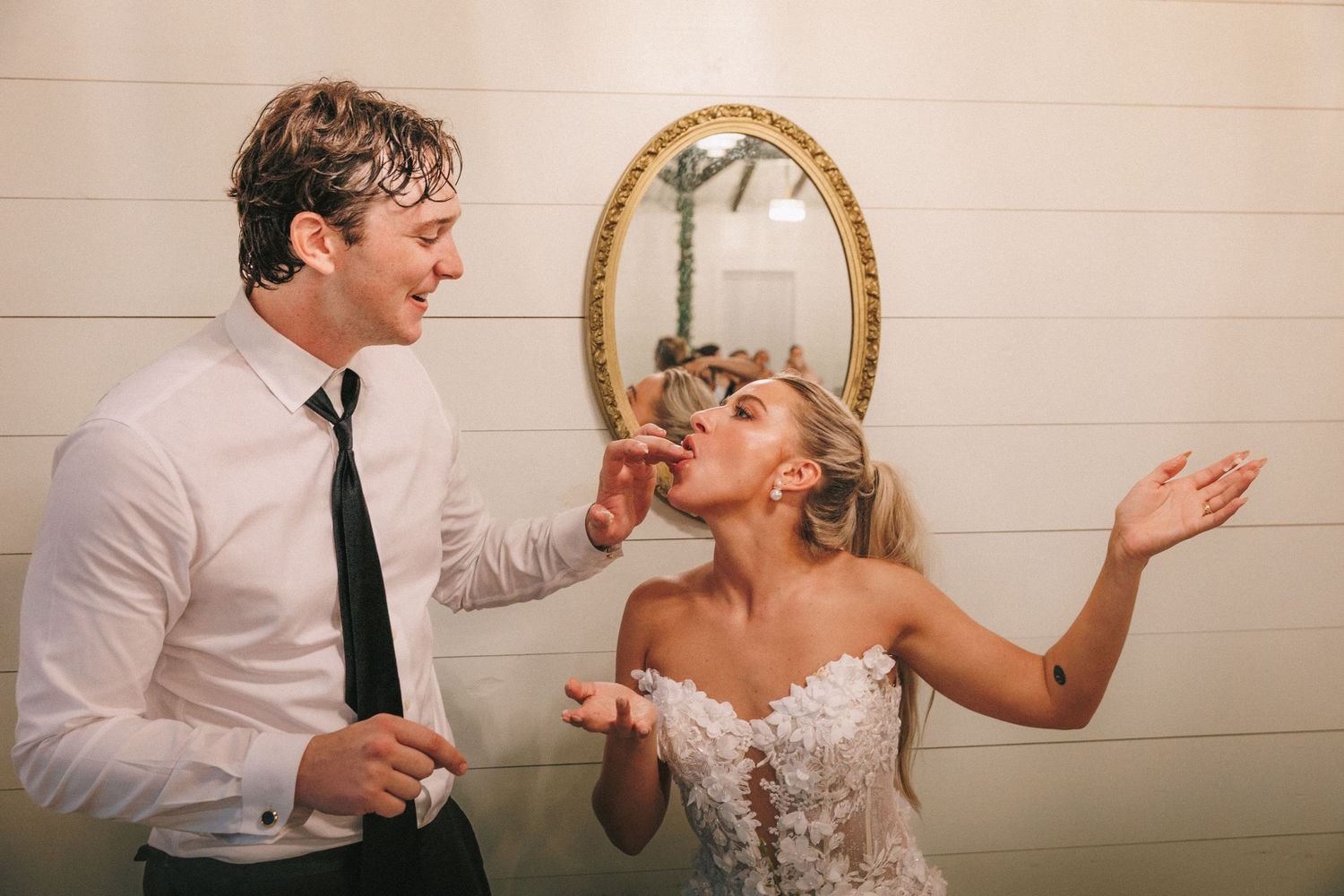 A playful wedding cake smash sequence showing the couple feeding each other cake in a rustic indoor setting.