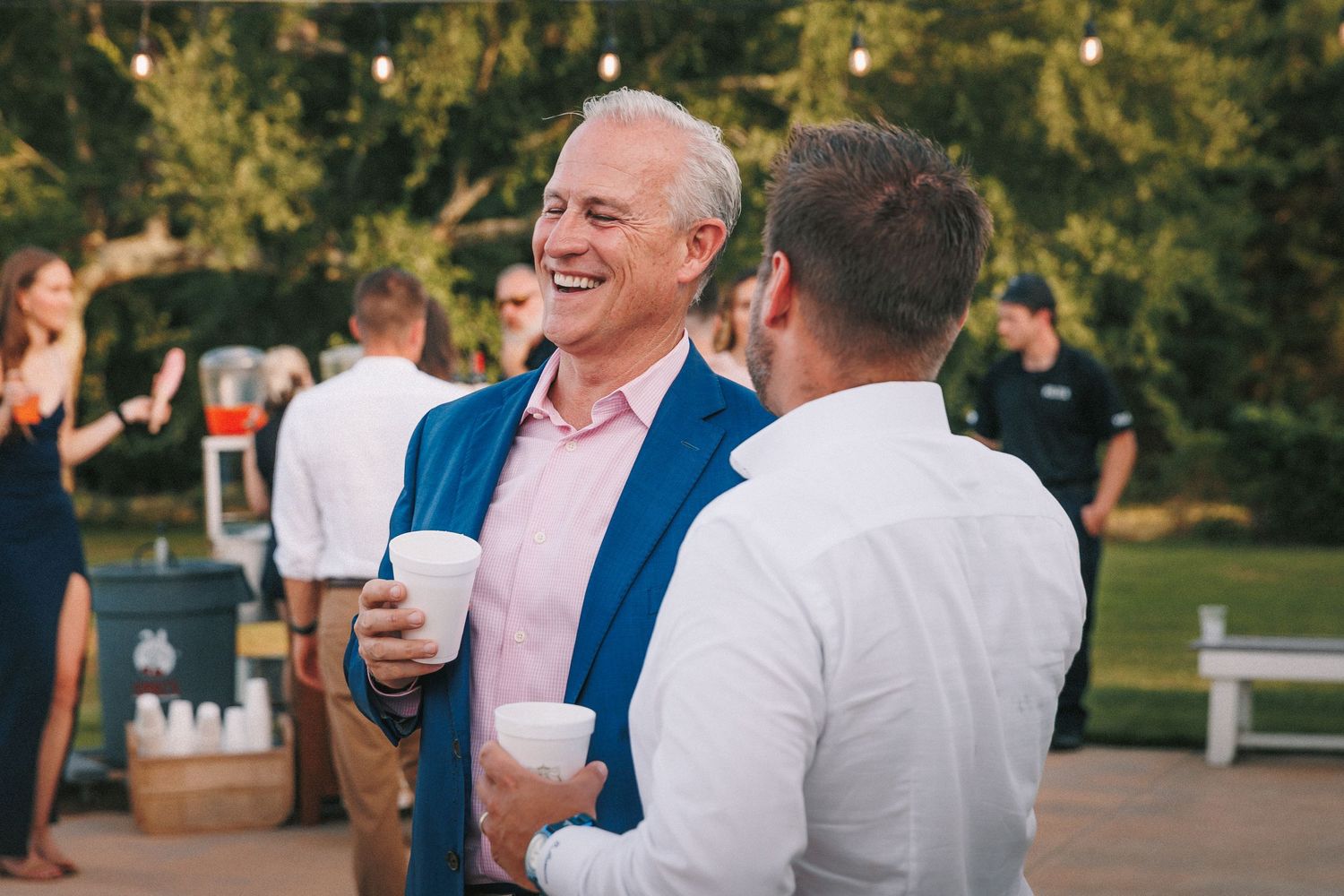 Wedding guests share drinks and laughter during an outdoor reception.
