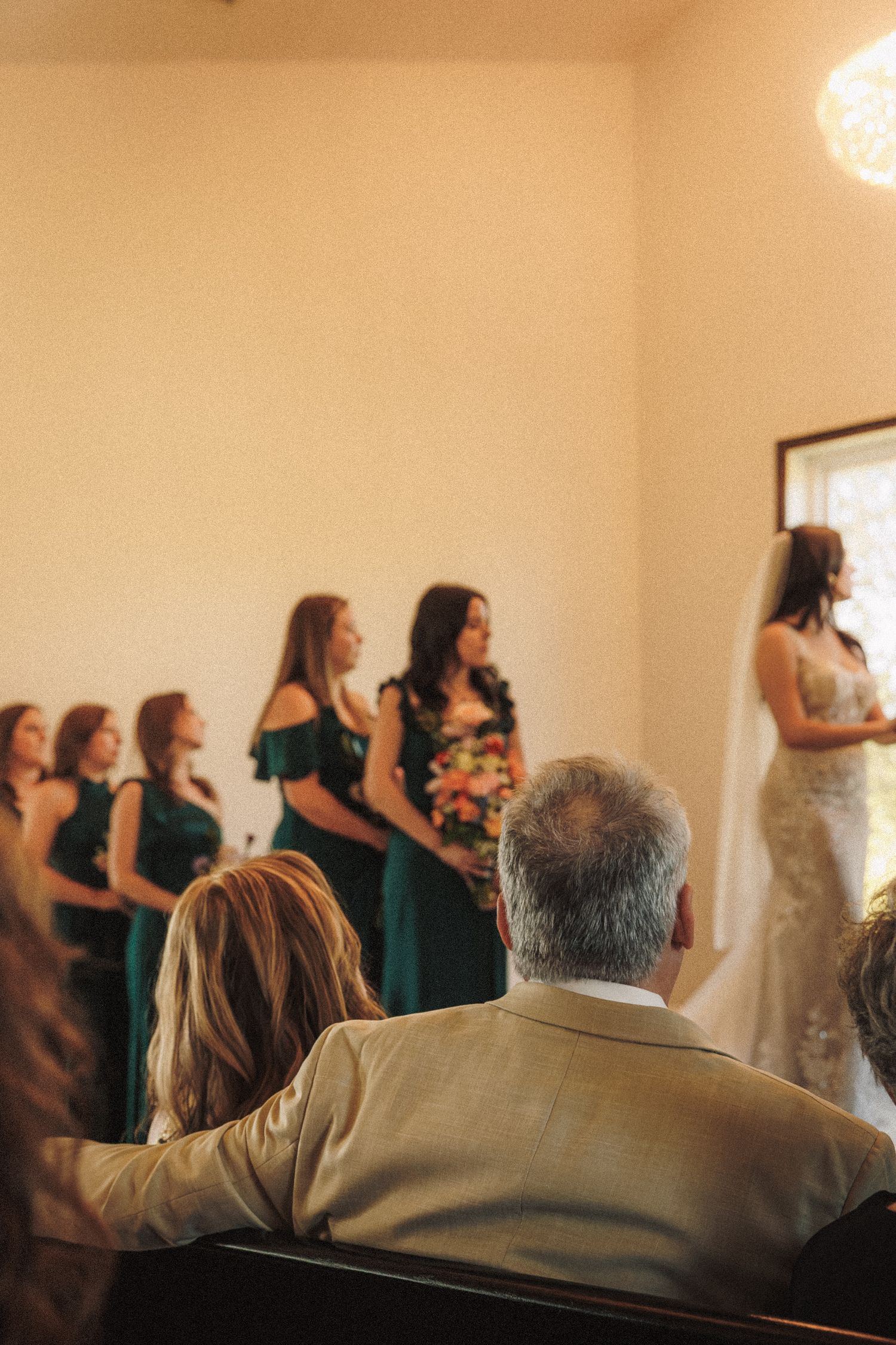 Bridesmaids in emerald green dresses stand at altar during wedding ceremony.
