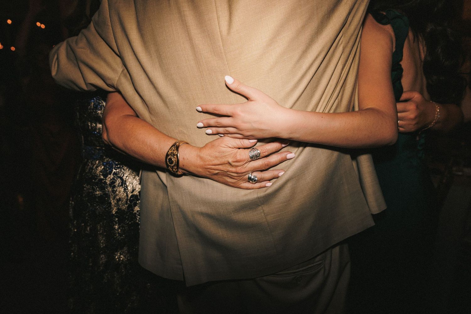 Close-up of hands embracing around a dancer wearing a beige outfit, with a diamond ring visible.
