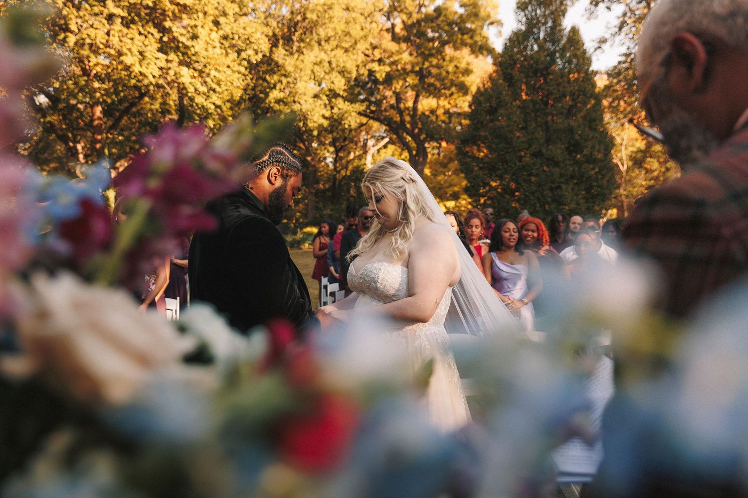 Bride and groom facing each other at an outdoor wedding ceremony surrounded by colorful autumn foliage and flowers.