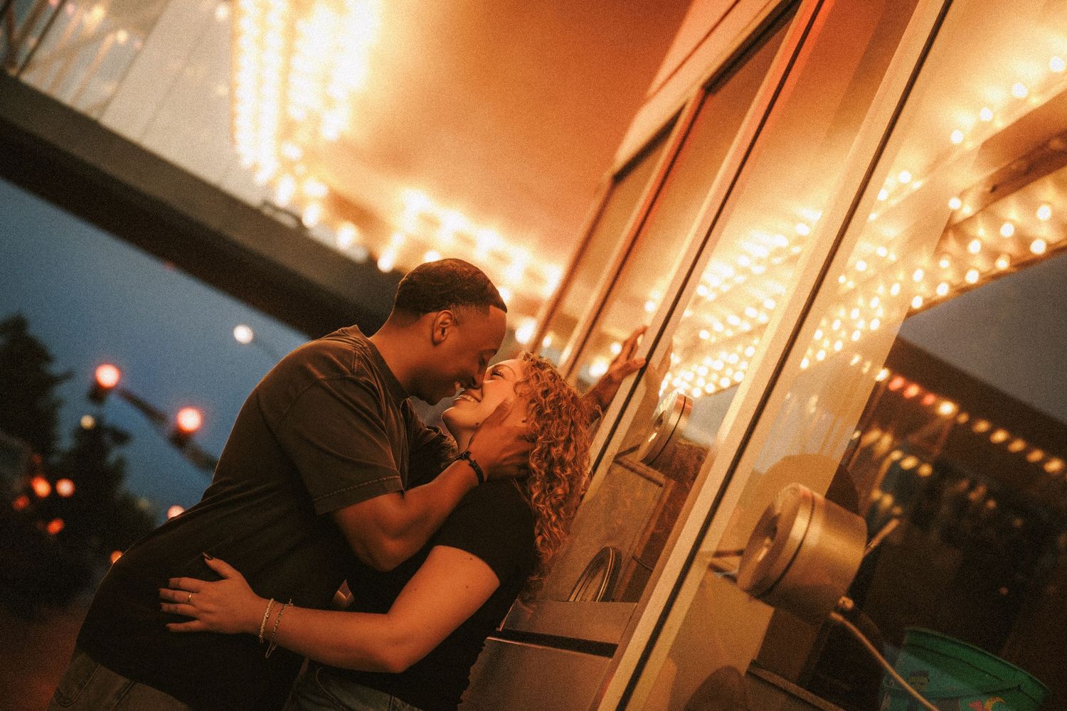 A romantic couple shares an intimate kiss against a mirrored wall illuminated by warm glowing lights in an evening setting.
