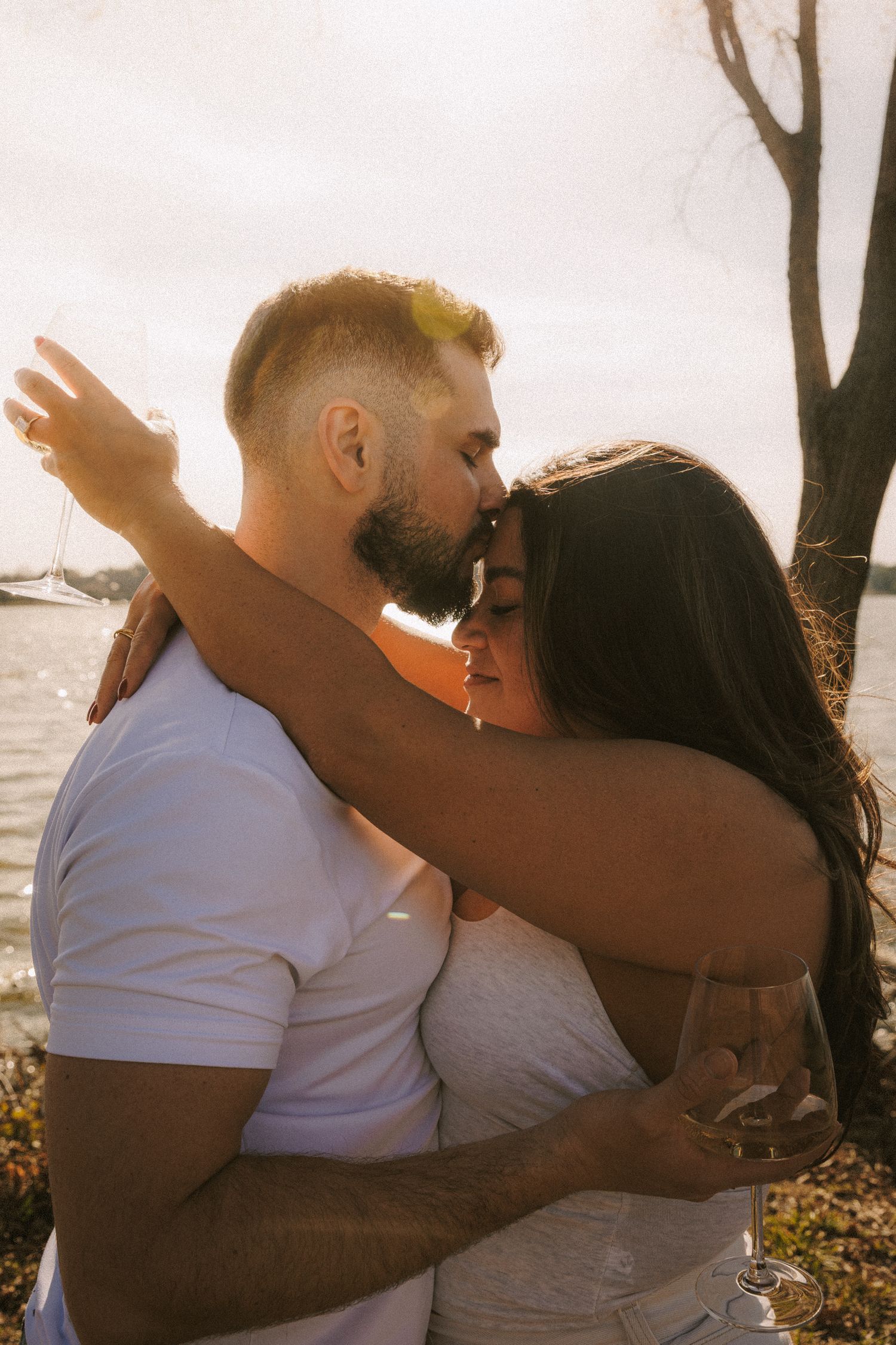 Romantic couple in white outfits share intimate moments during a golden hour photoshoot by the water.
