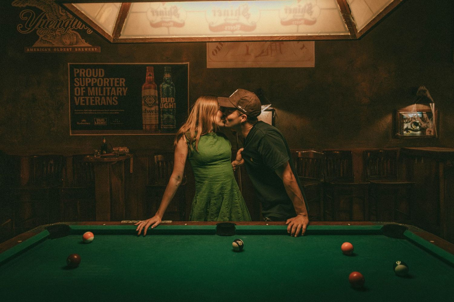 Players enjoy a game of billiards in a dimly lit pool hall with warm lighting and vintage atmosphere.