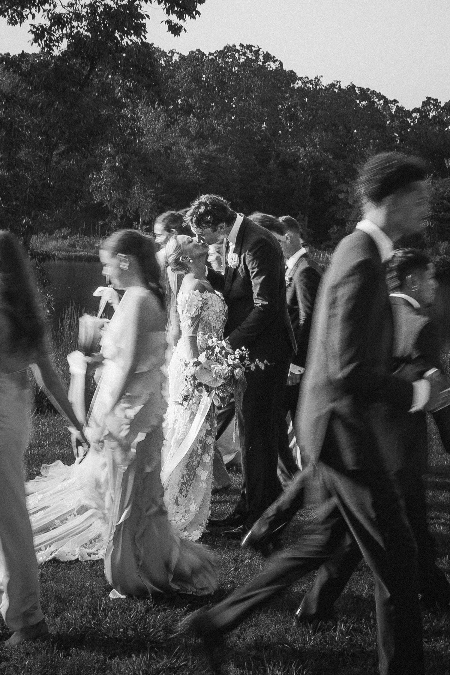 Wedding party walks together across outdoor venue in black and white photograph.