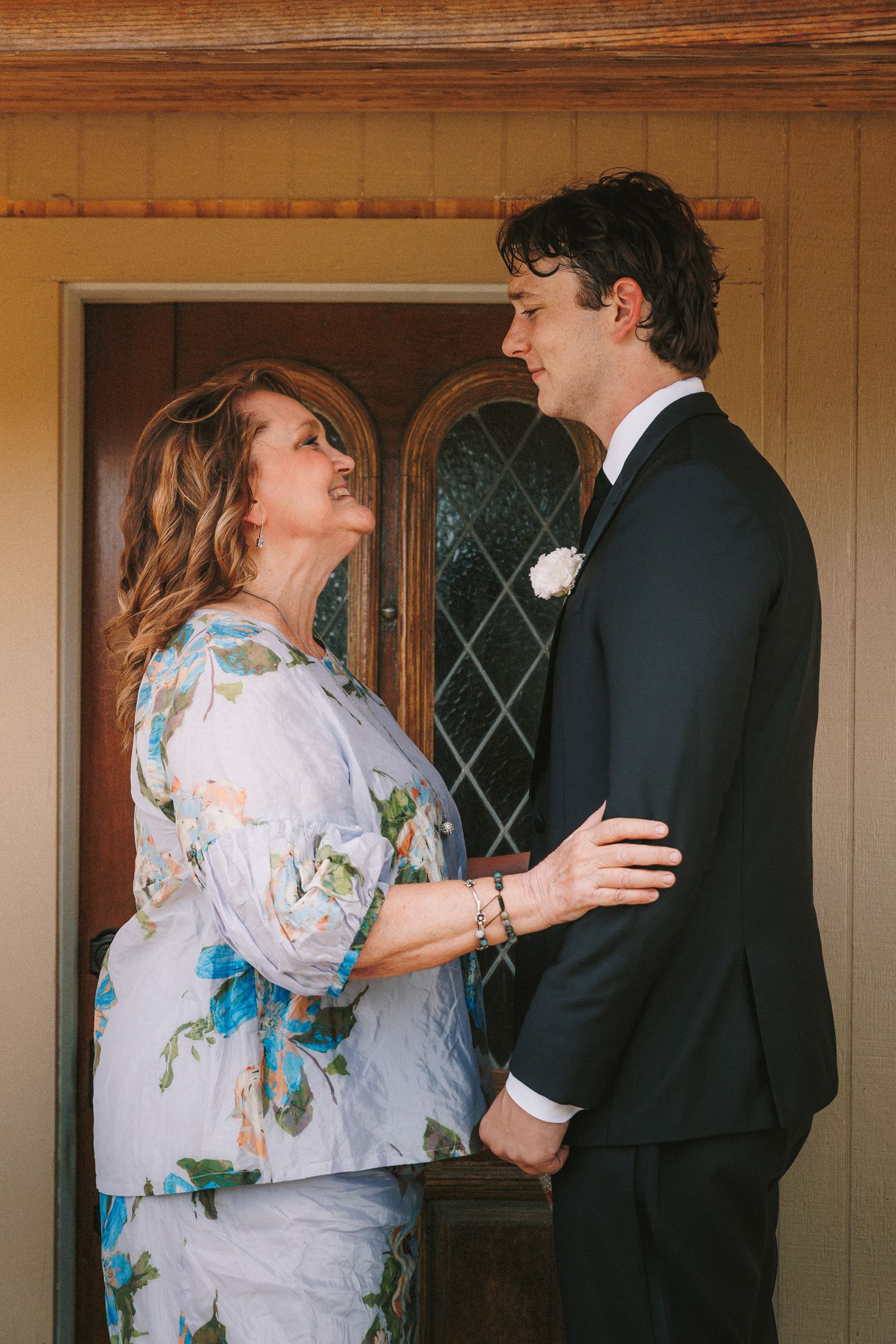 Couple in contrasting formal wear sharing an intimate moment in a rustic indoor setting.