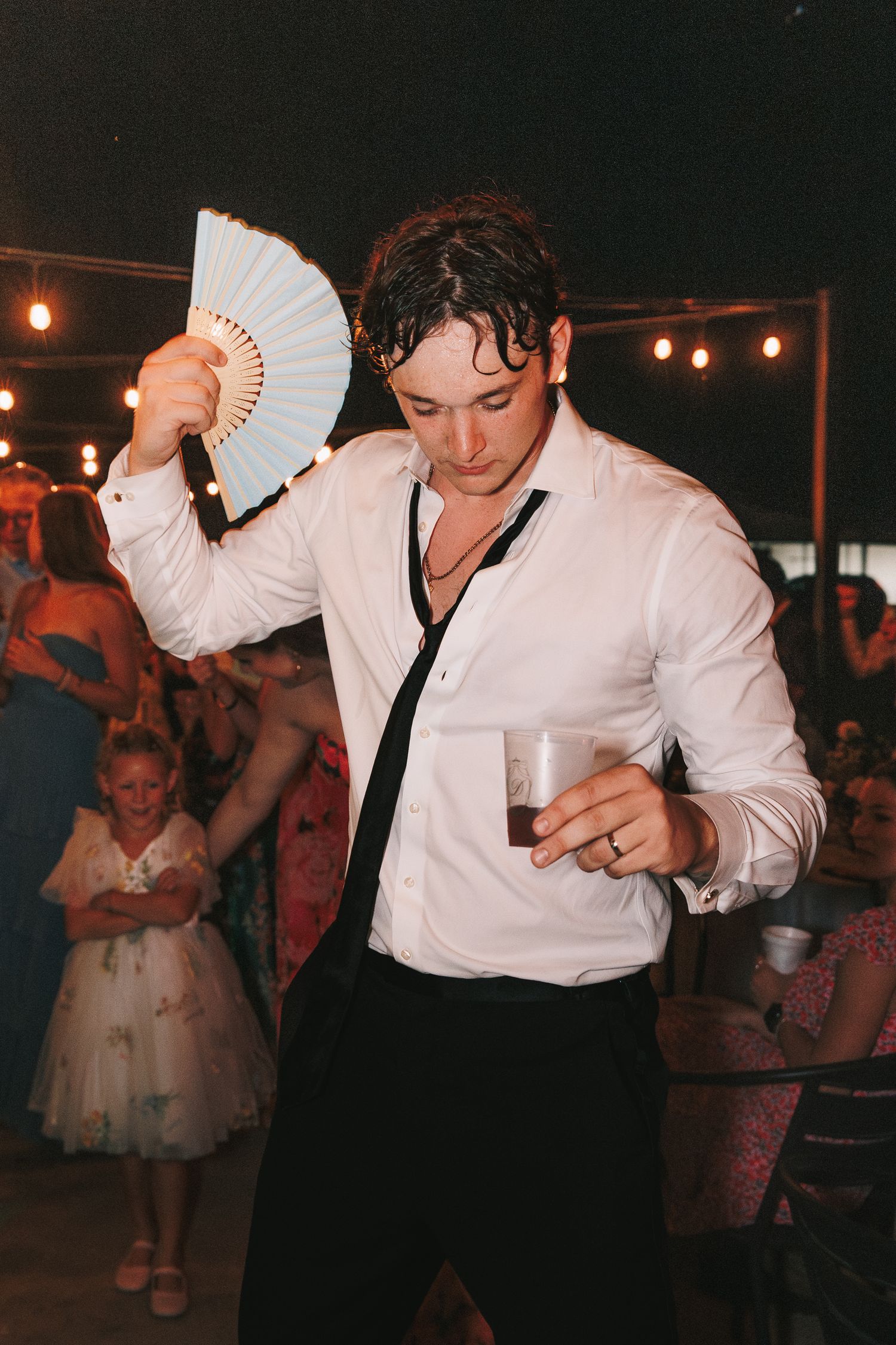 People dancing and celebrating at a dimly lit party with string lights overhead.