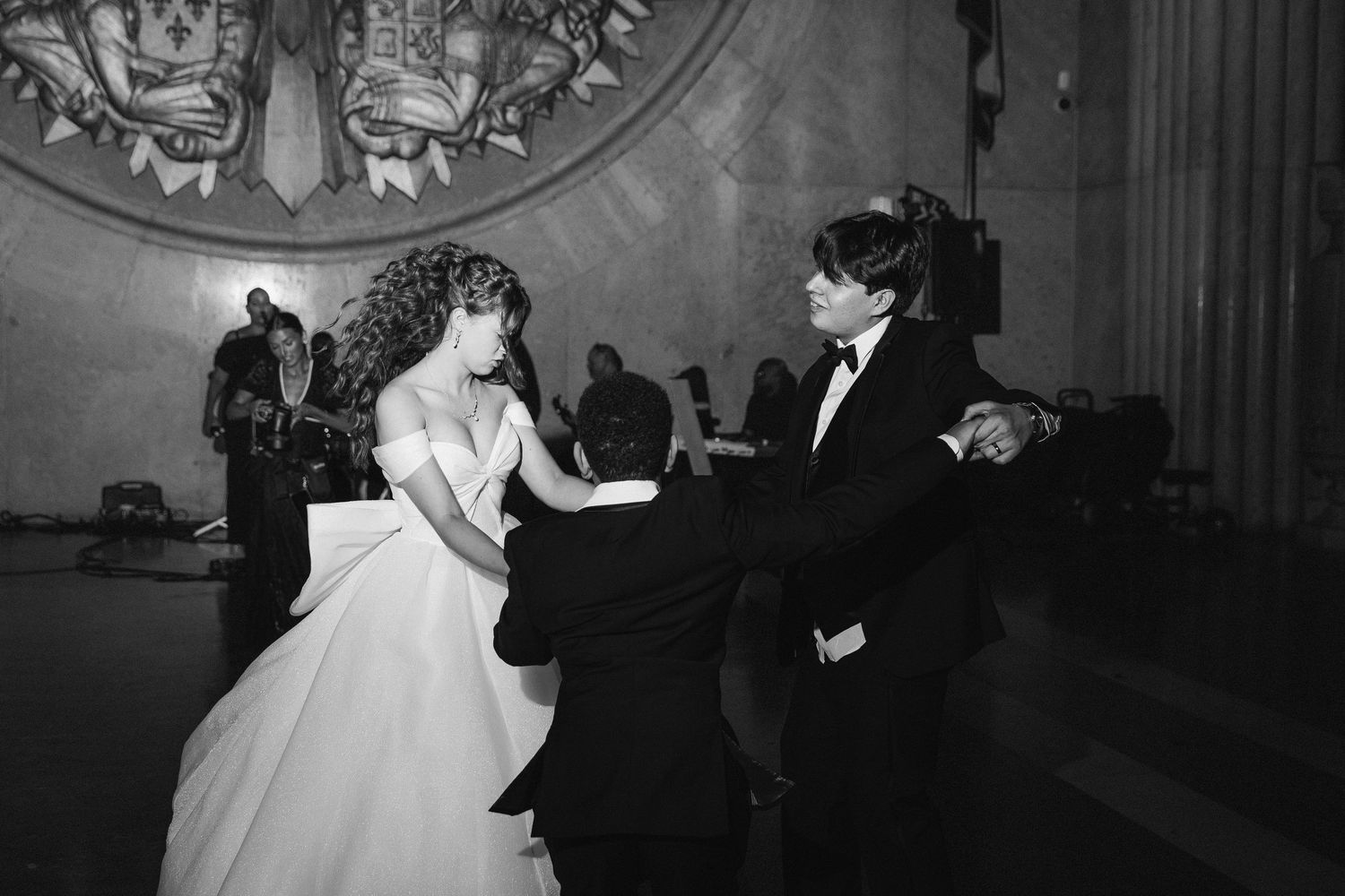 Black and white photo of bride and groom sharing first dance in ornate ballroom.