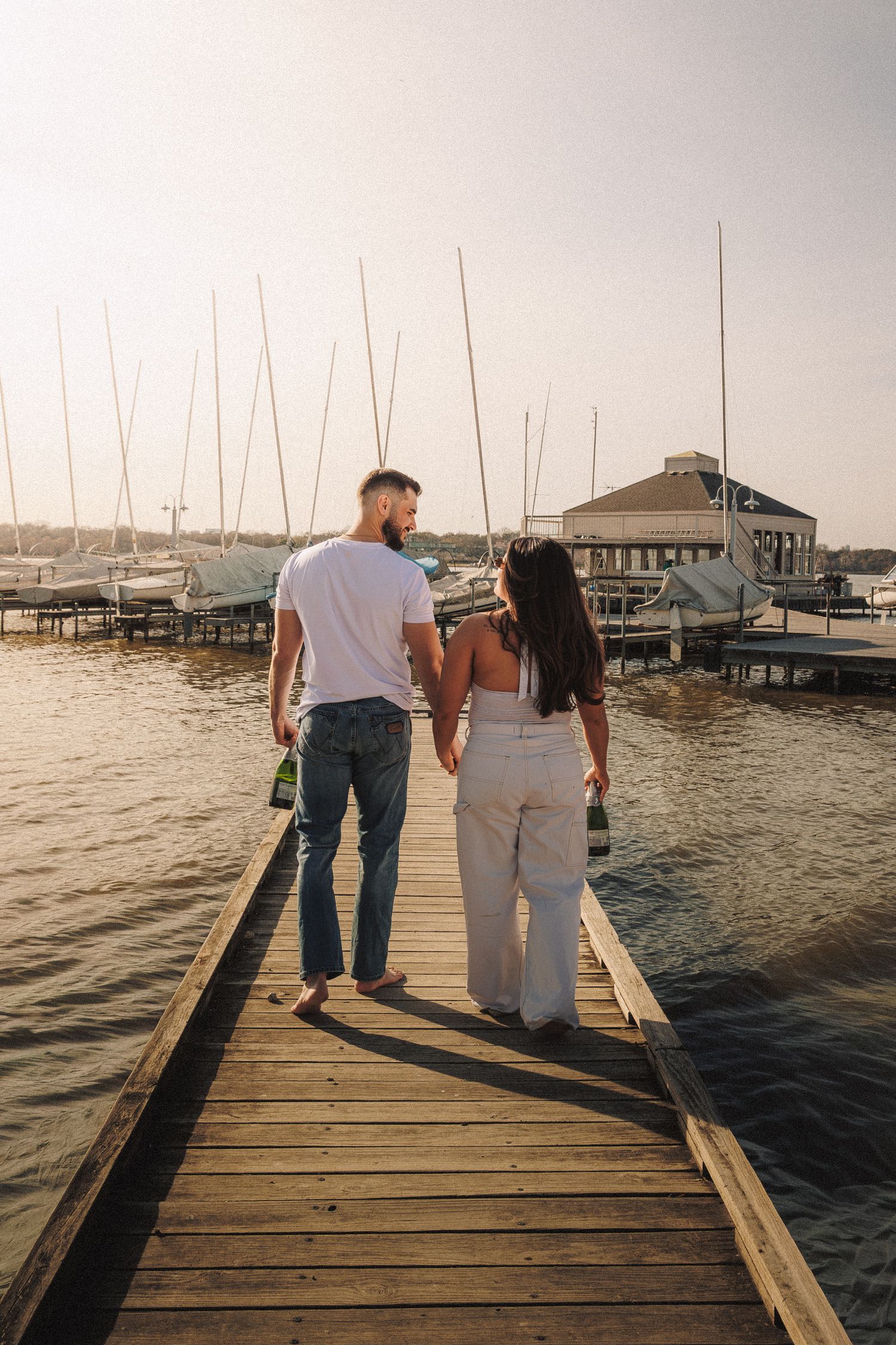 People walking along a wooden dock with boats and marina in the background at dusk.