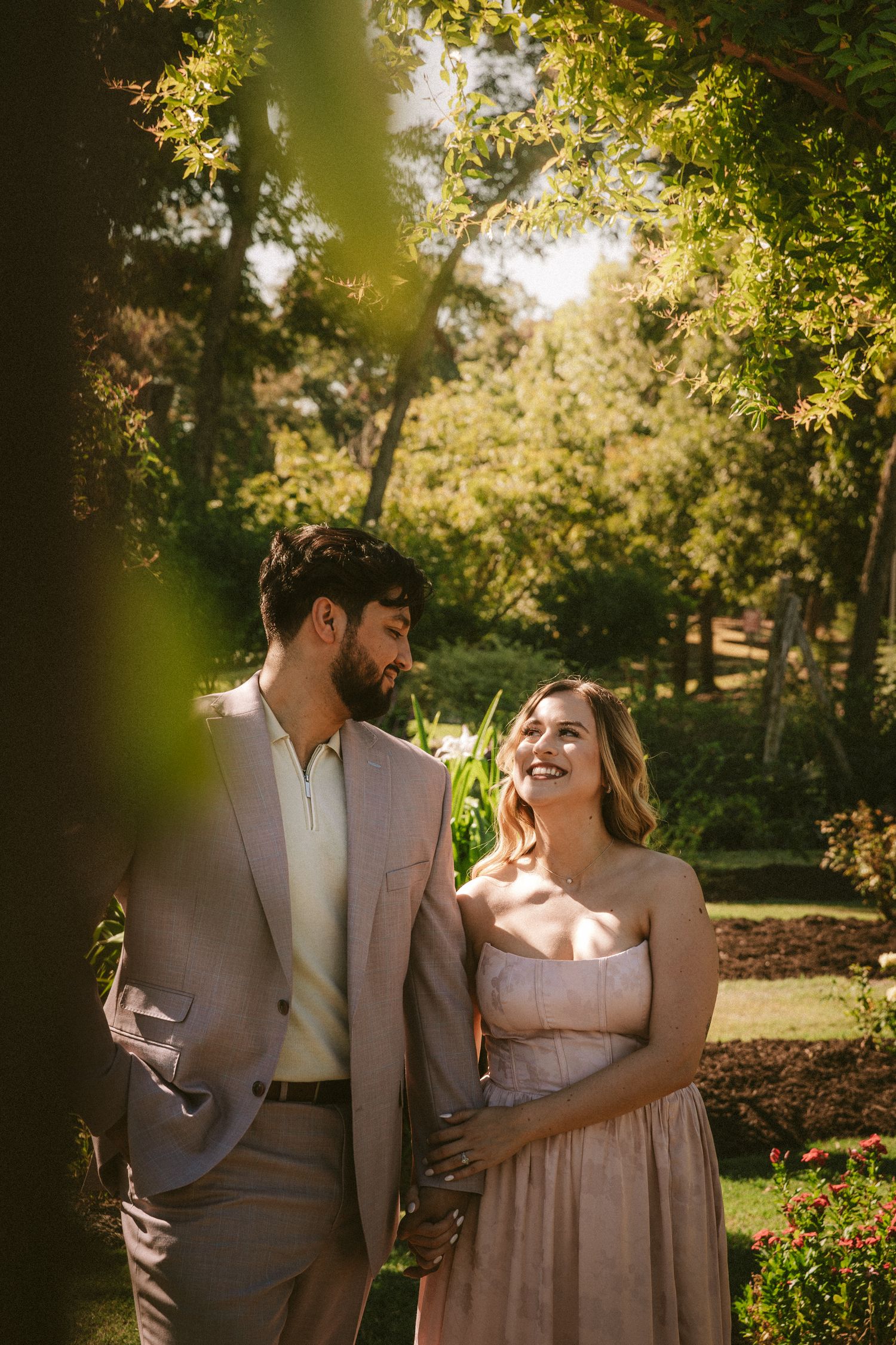 A couple shares joyful moments together in a sunlit garden setting during a romantic outdoor photoshoot.