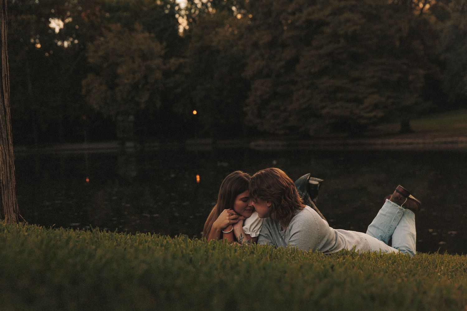Couple lying together in a grassy field during golden hour sunset.