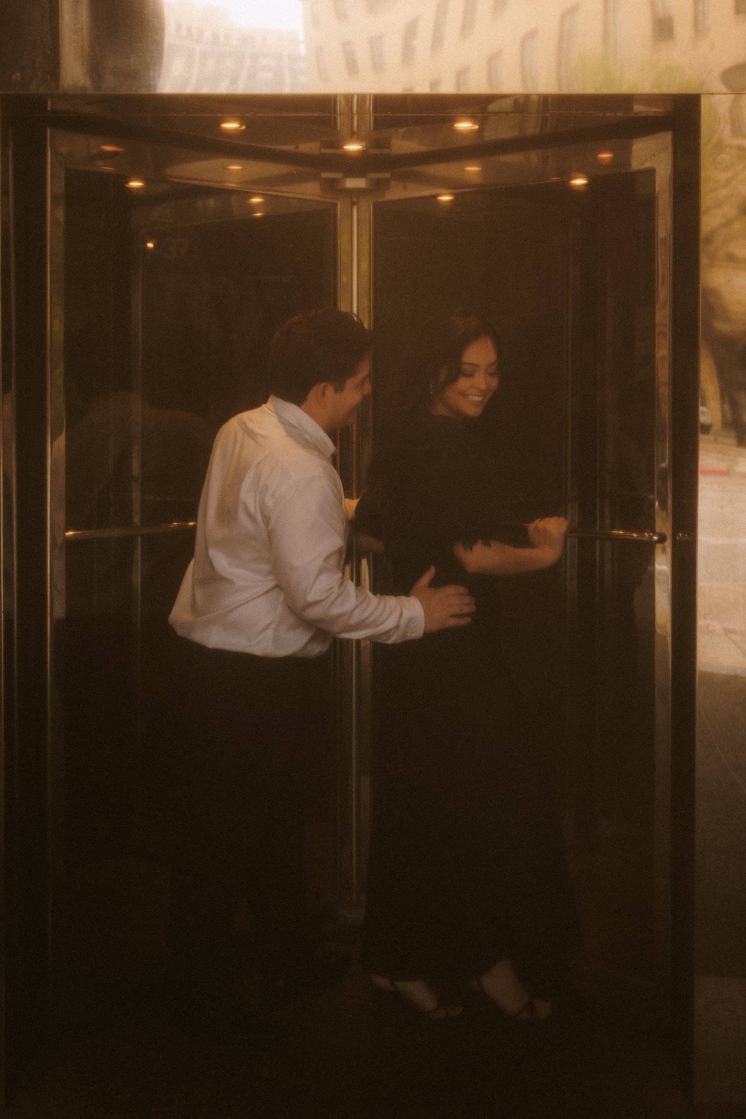 Couple sharing a romantic moment inside a golden elevator with reflective doors.