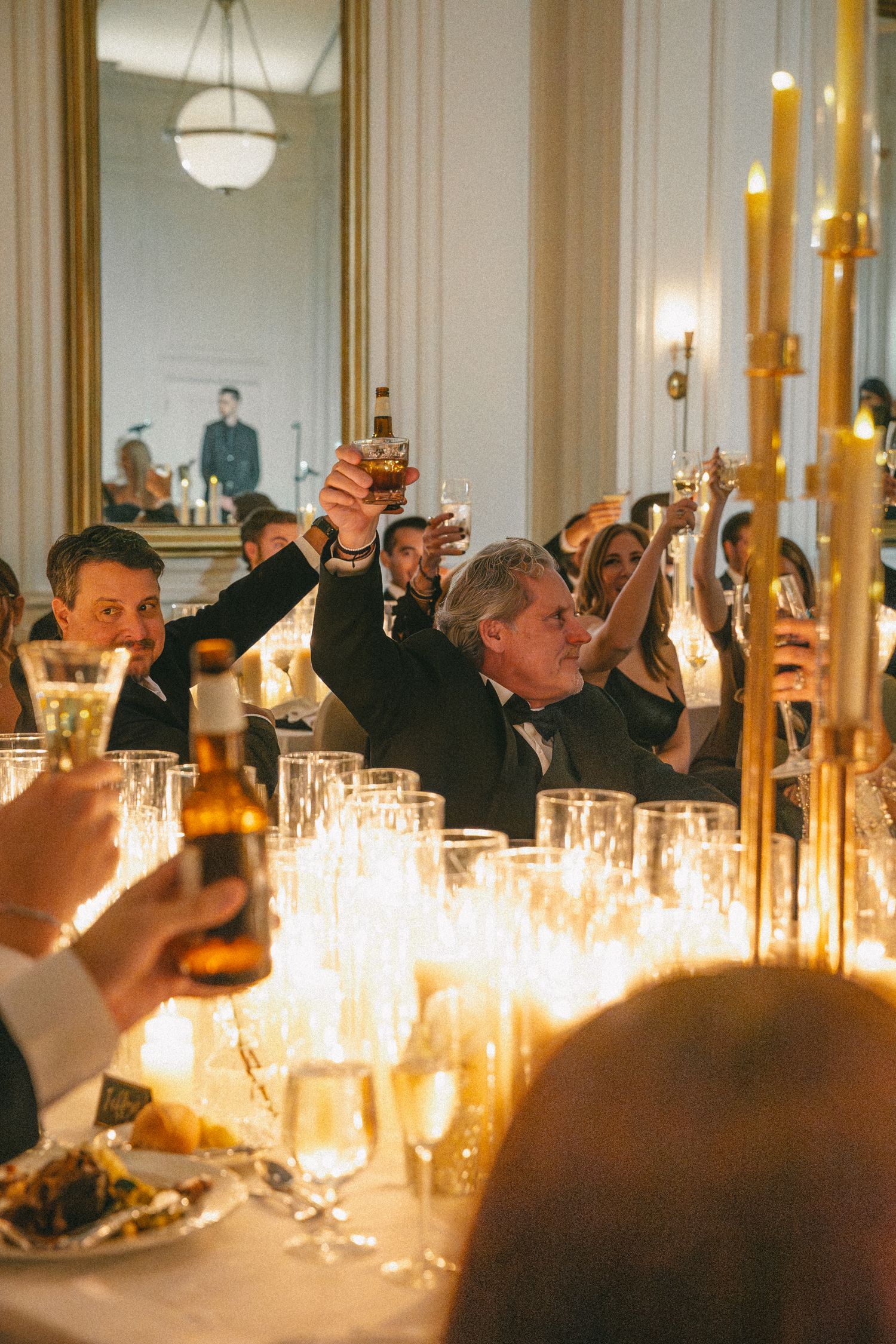 Wedding guests raise glasses in a champagne toast at an elegant candlelit reception dinner.