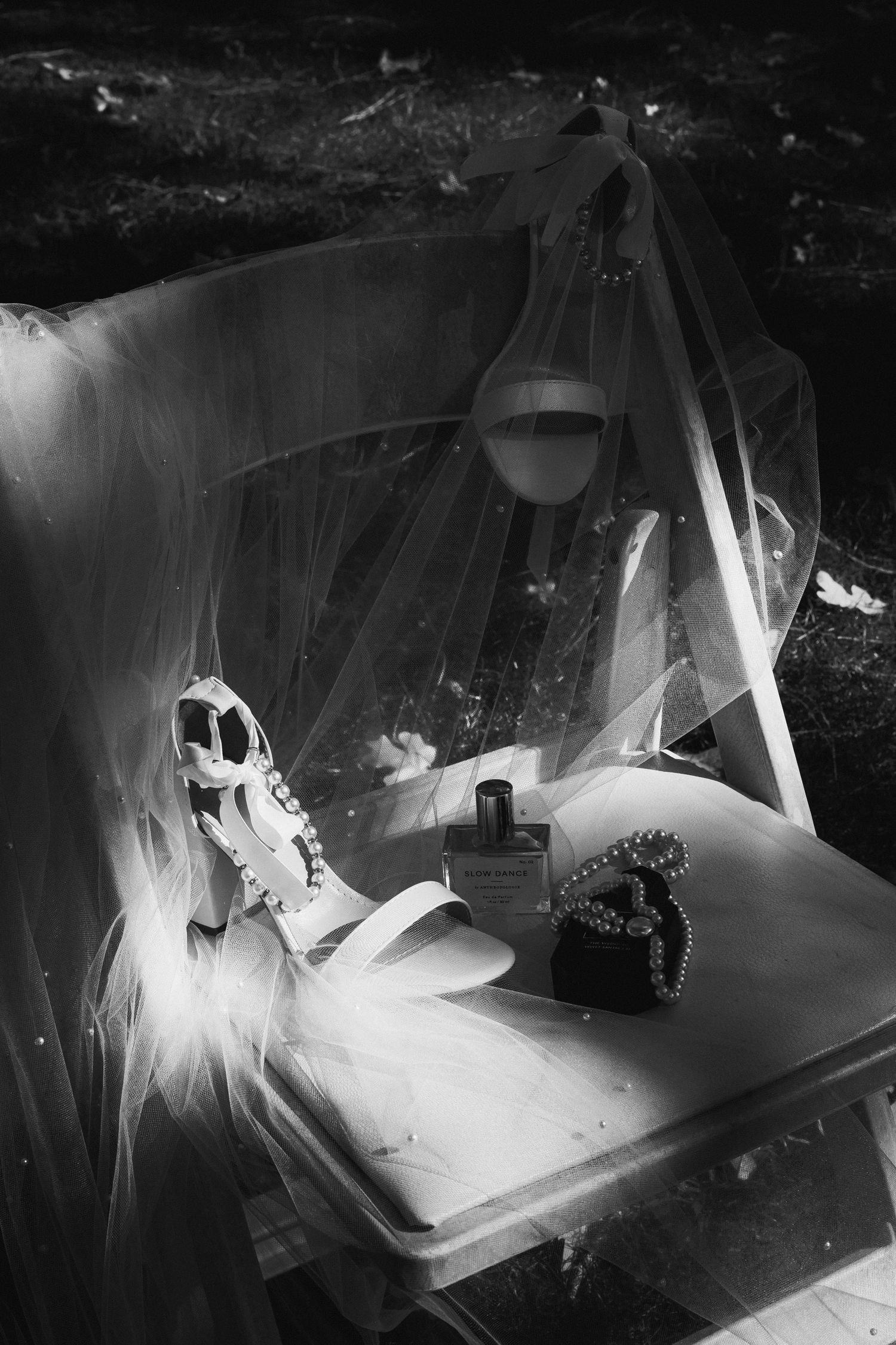 Black and white photo of a skull, perfume bottle, and heart jewelry box on a table draped with a bridal veil.