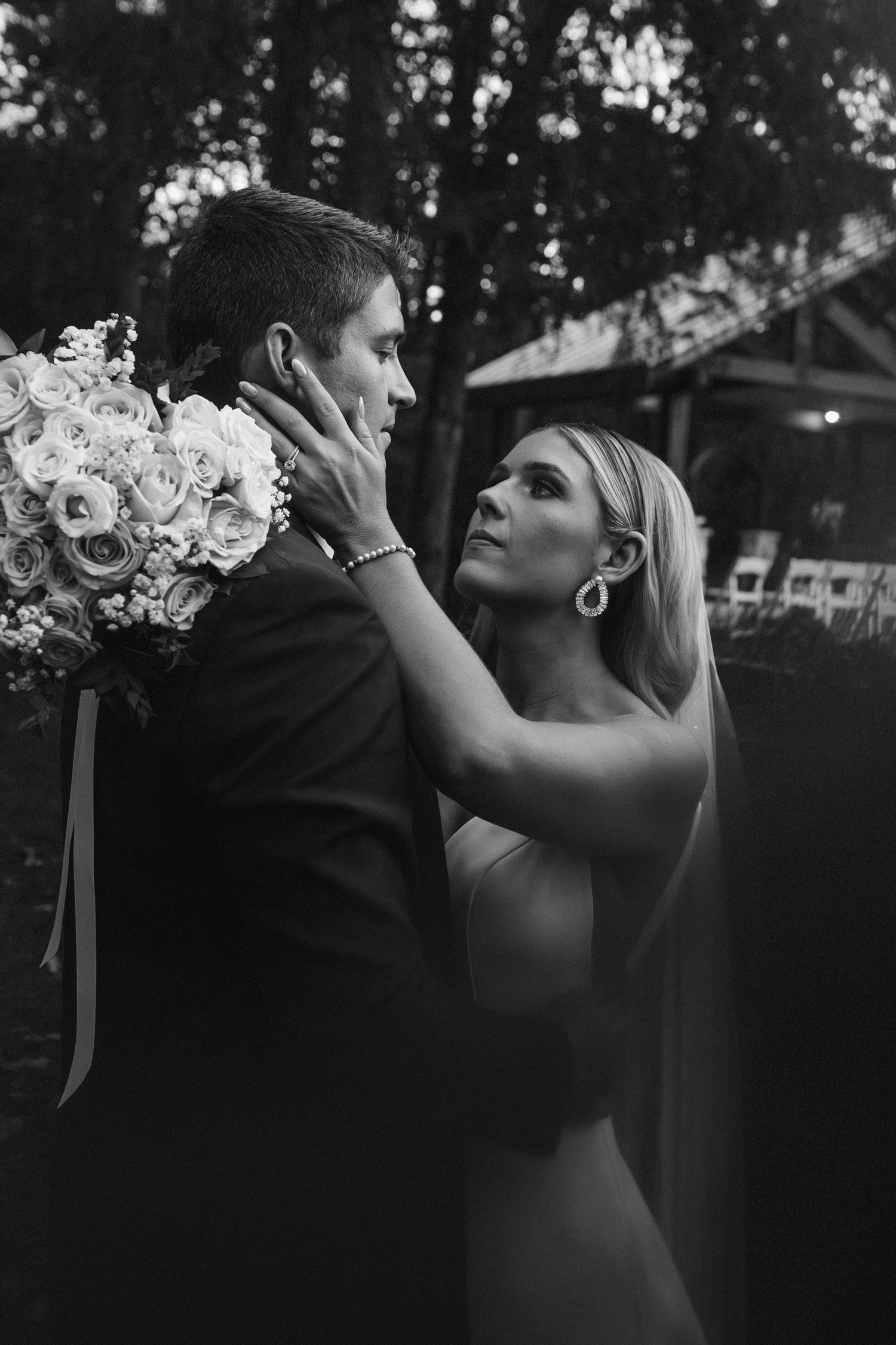 Black and white romantic portrait of bride gazing at groom while holding white rose bouquet.