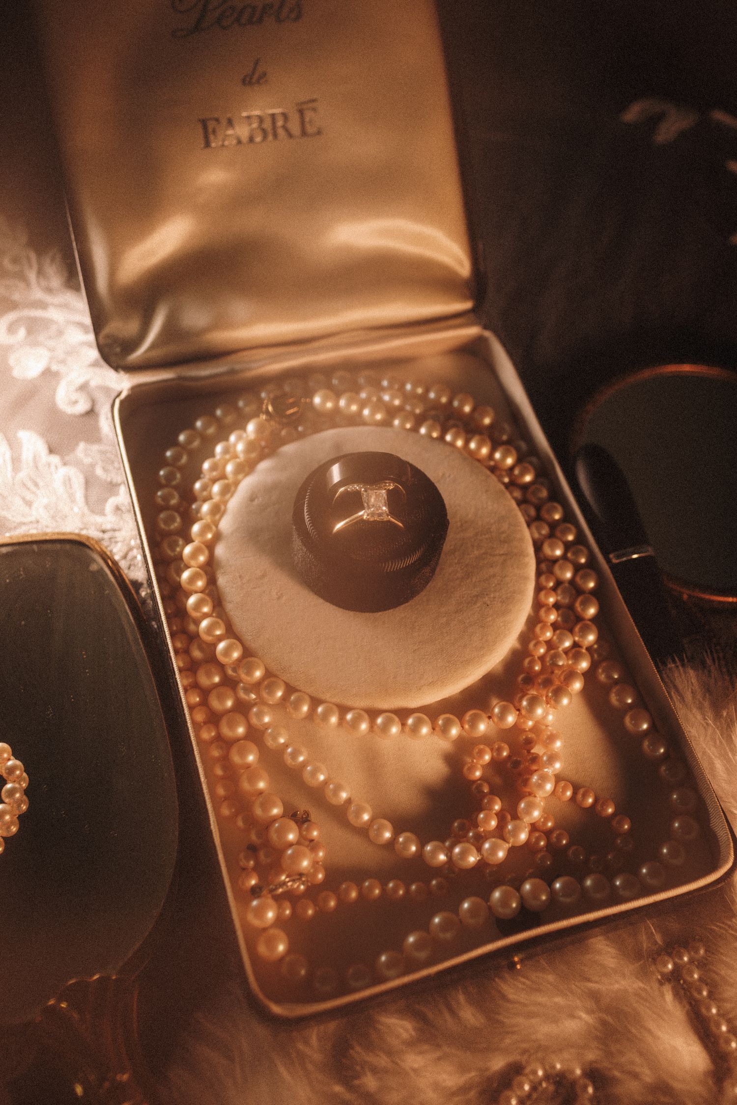 Vintage gold tin box with pearl necklaces and diamond engagement ring on velvet cushion.