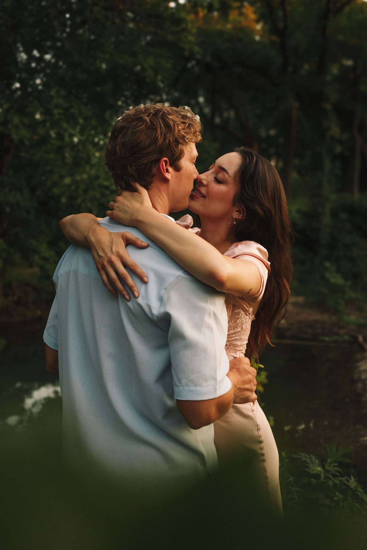 Romantic couple sharing an intimate kiss in a natural outdoor setting near a lake at golden hour.
