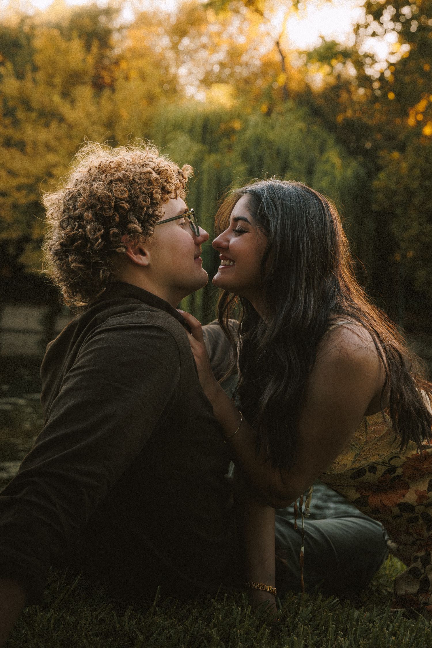 Two people share an intimate moment outdoors during sunset with trees in the background.