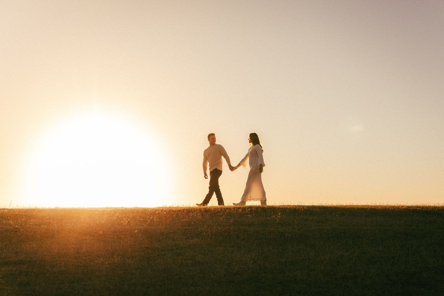 Dallas, Texas Engagement PhotographerTwo silhouetted figures stand together against a warm sunset sky on a hilltop horizon.