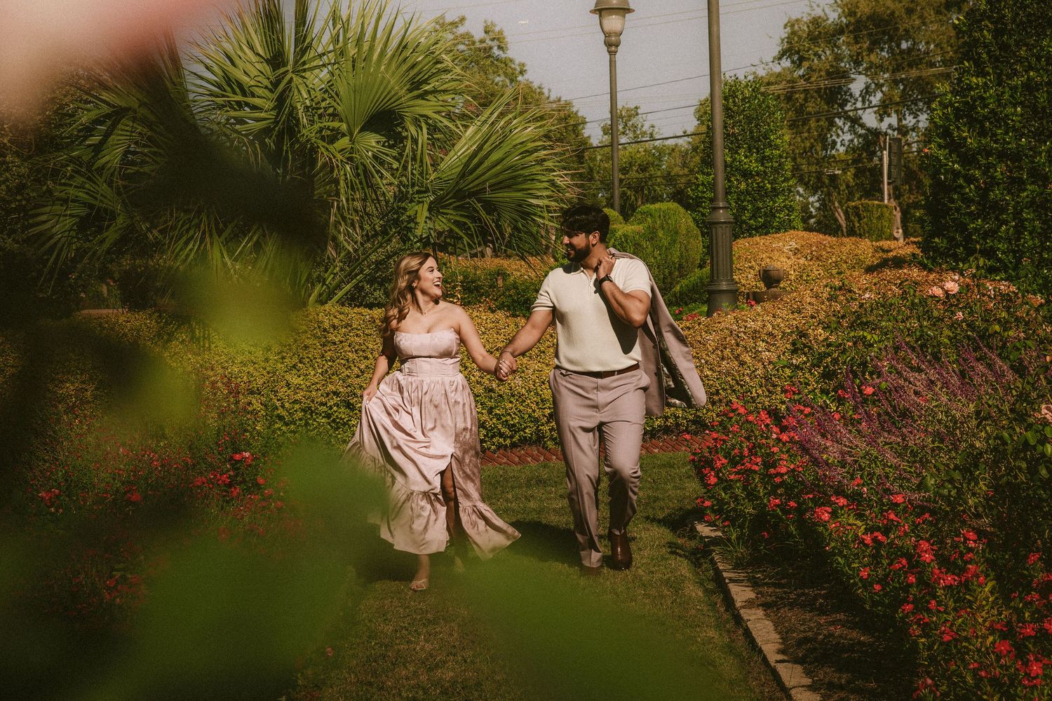 A couple walking through a garden path surrounded by blooming flowers at sunset.