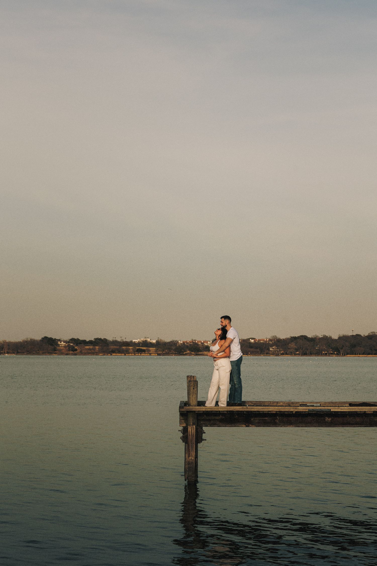 Couple sits on wooden pier overlooking calm waters during sunset.