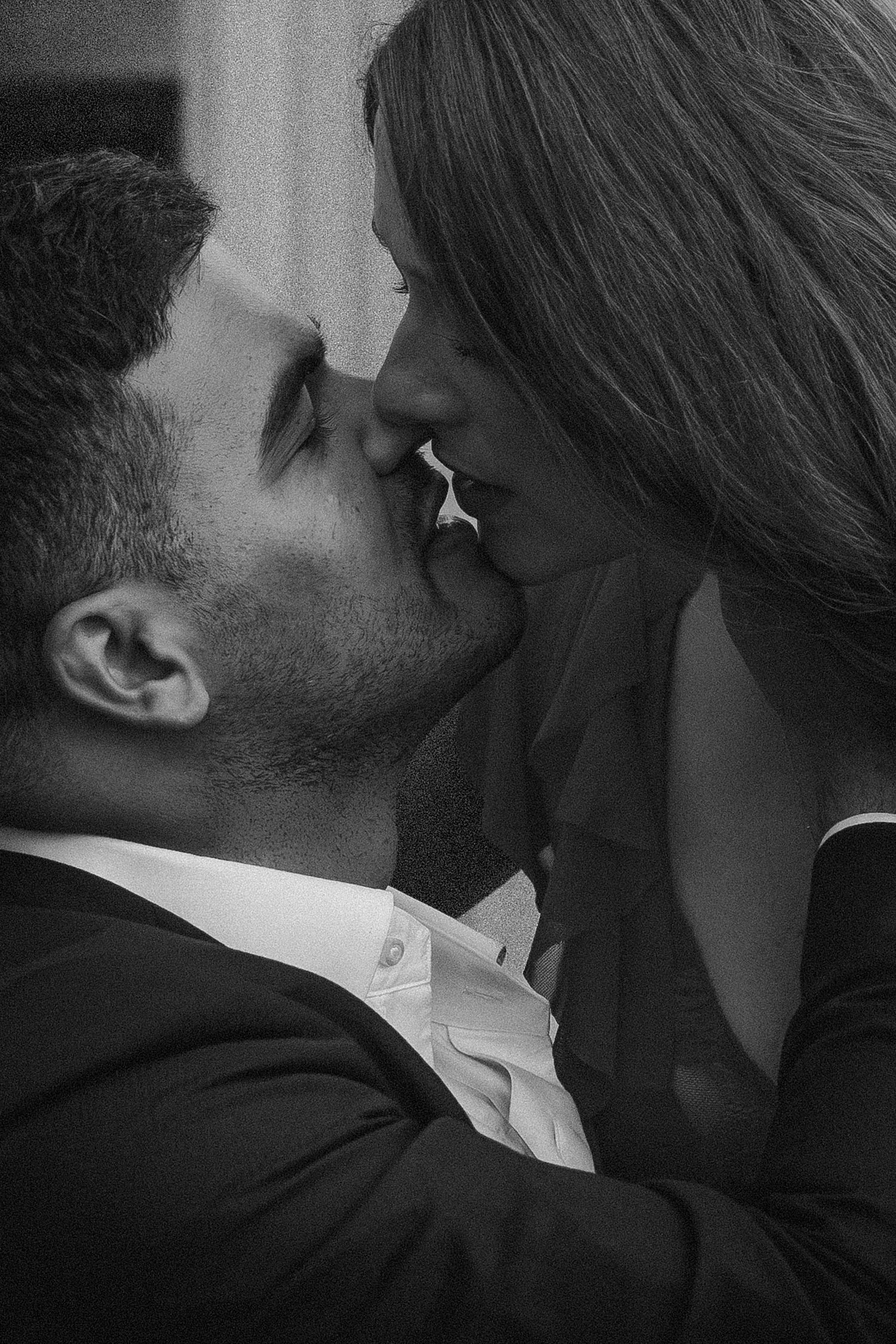 Black and white photo of a romantic couple sharing a tender kiss, man in suit, intimate close-up portrait.