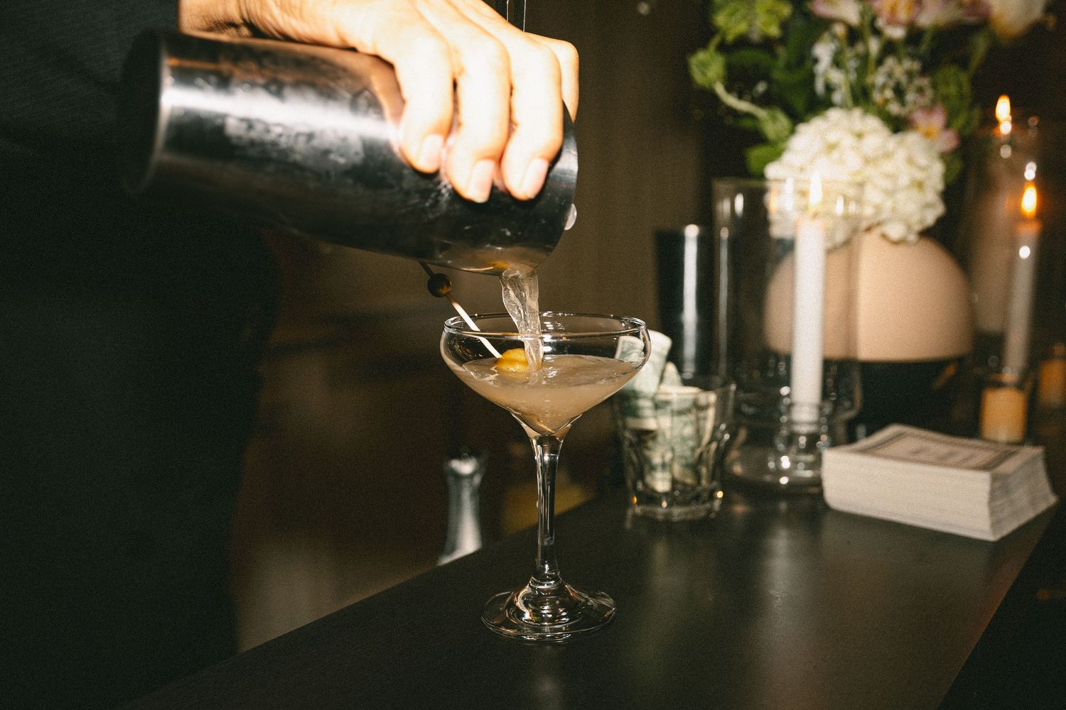 Bartender pouring an espresso martini cocktail into a coupe glass at a wedding reception bar.