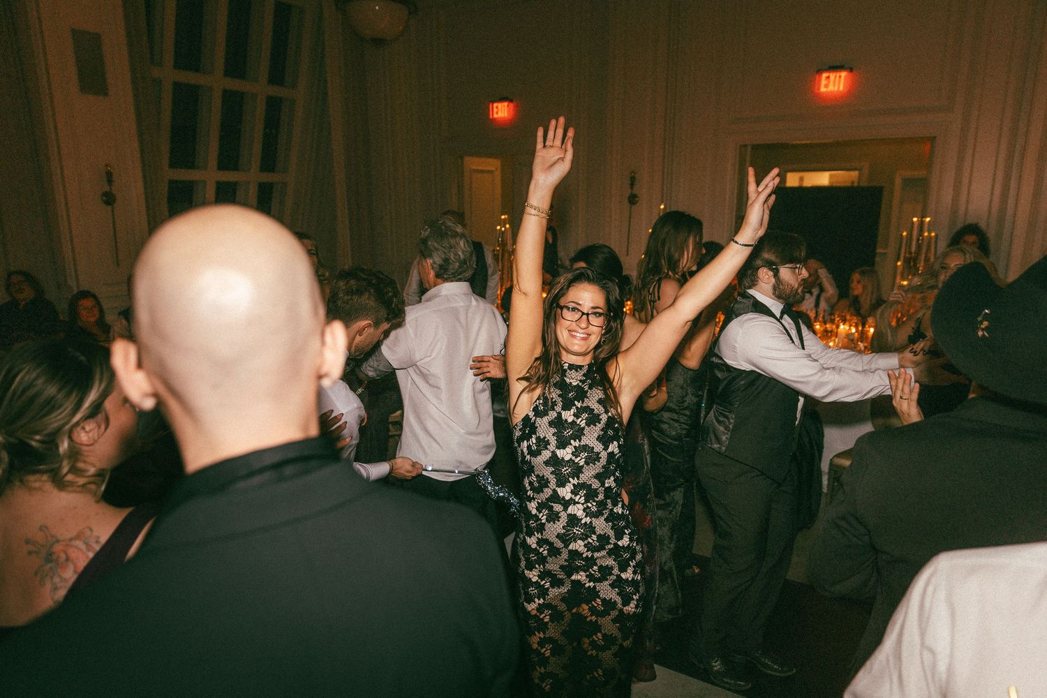 Guests dance and celebrate with raised hands on a crowded wedding reception dance floor.