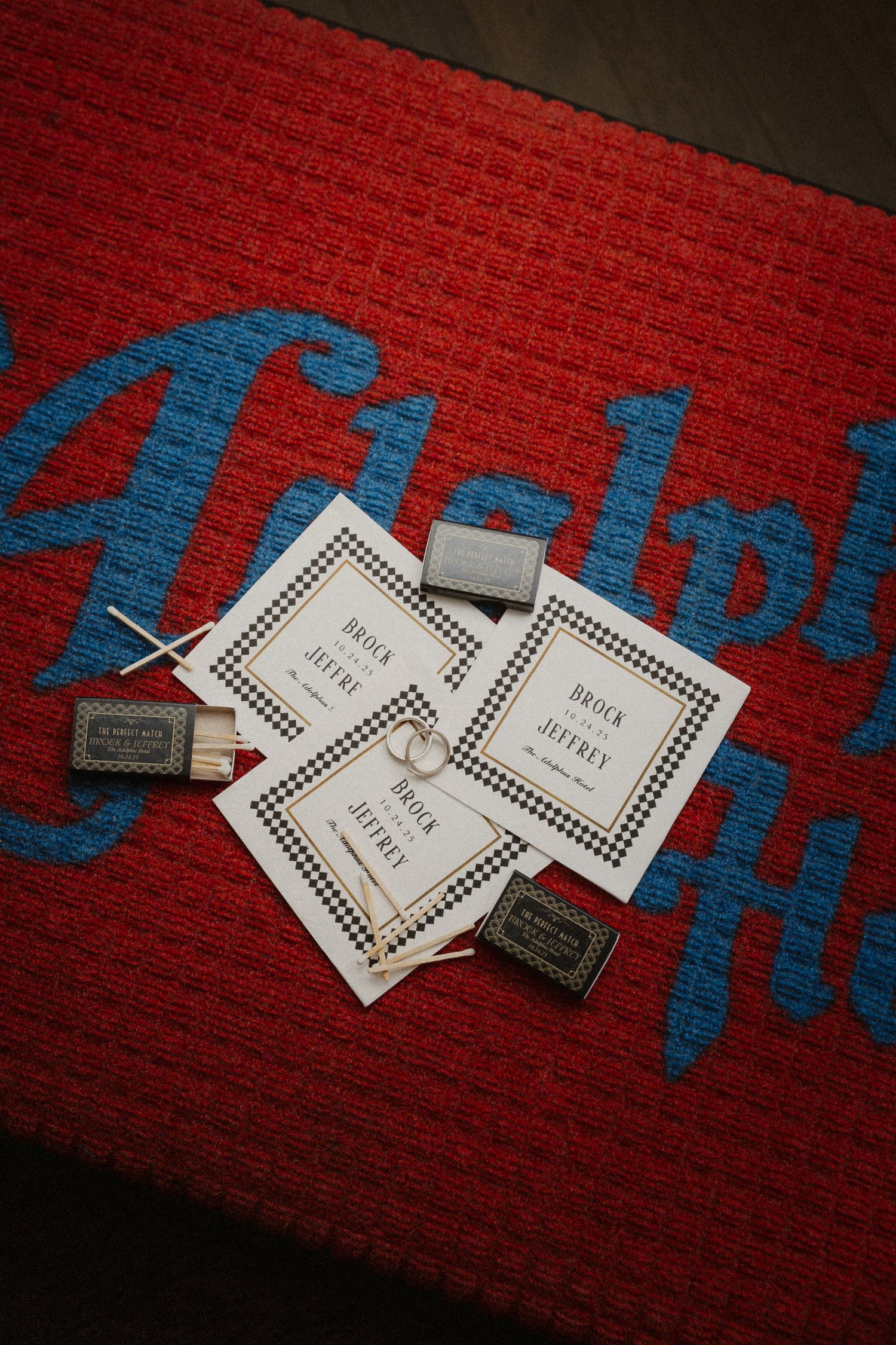 Wedding stationery with houndstooth borders for Brock and Jeffrey on a red rug with matchboxes.