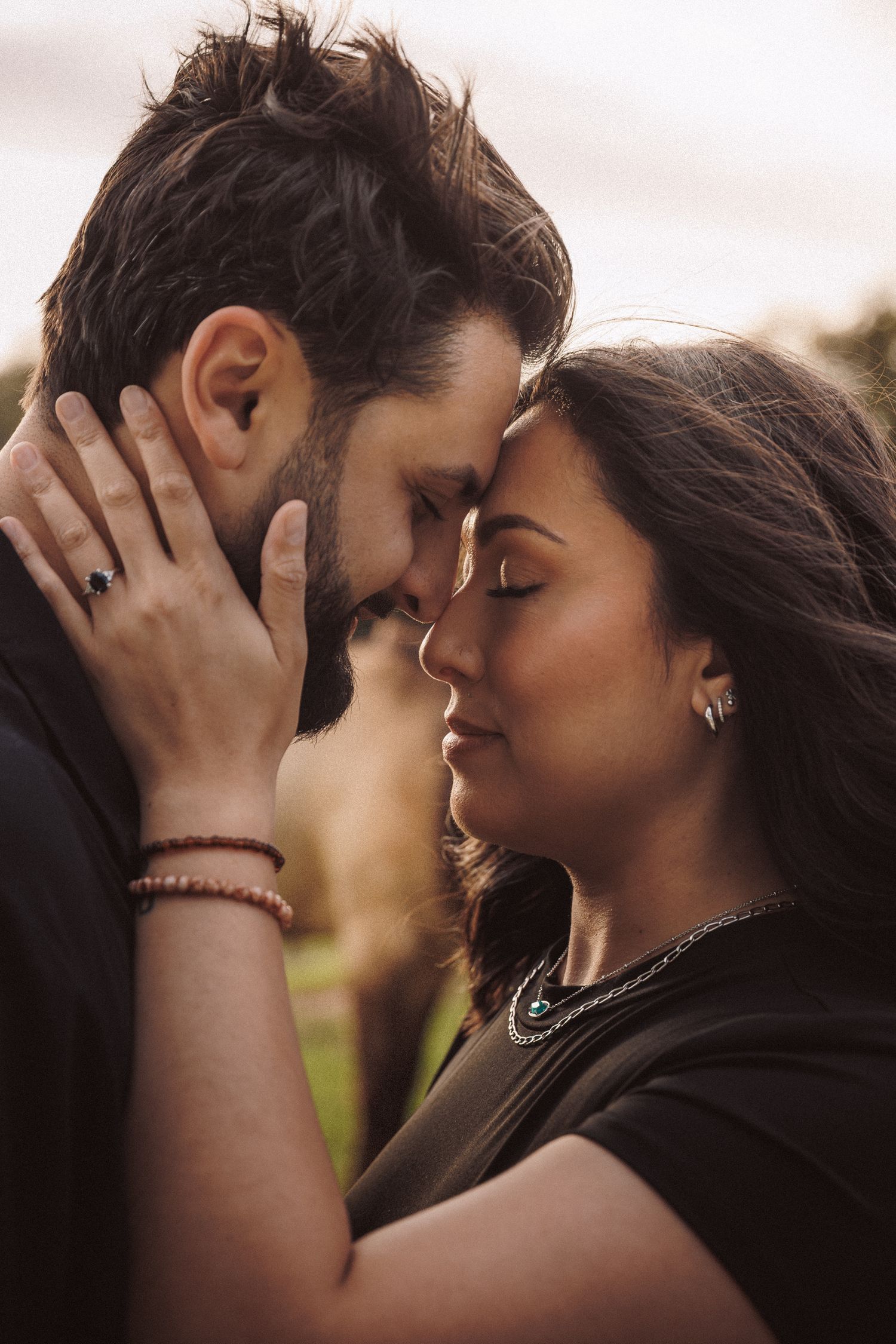 Romantic couple touching foreheads tenderly in a golden sunset outdoor setting.