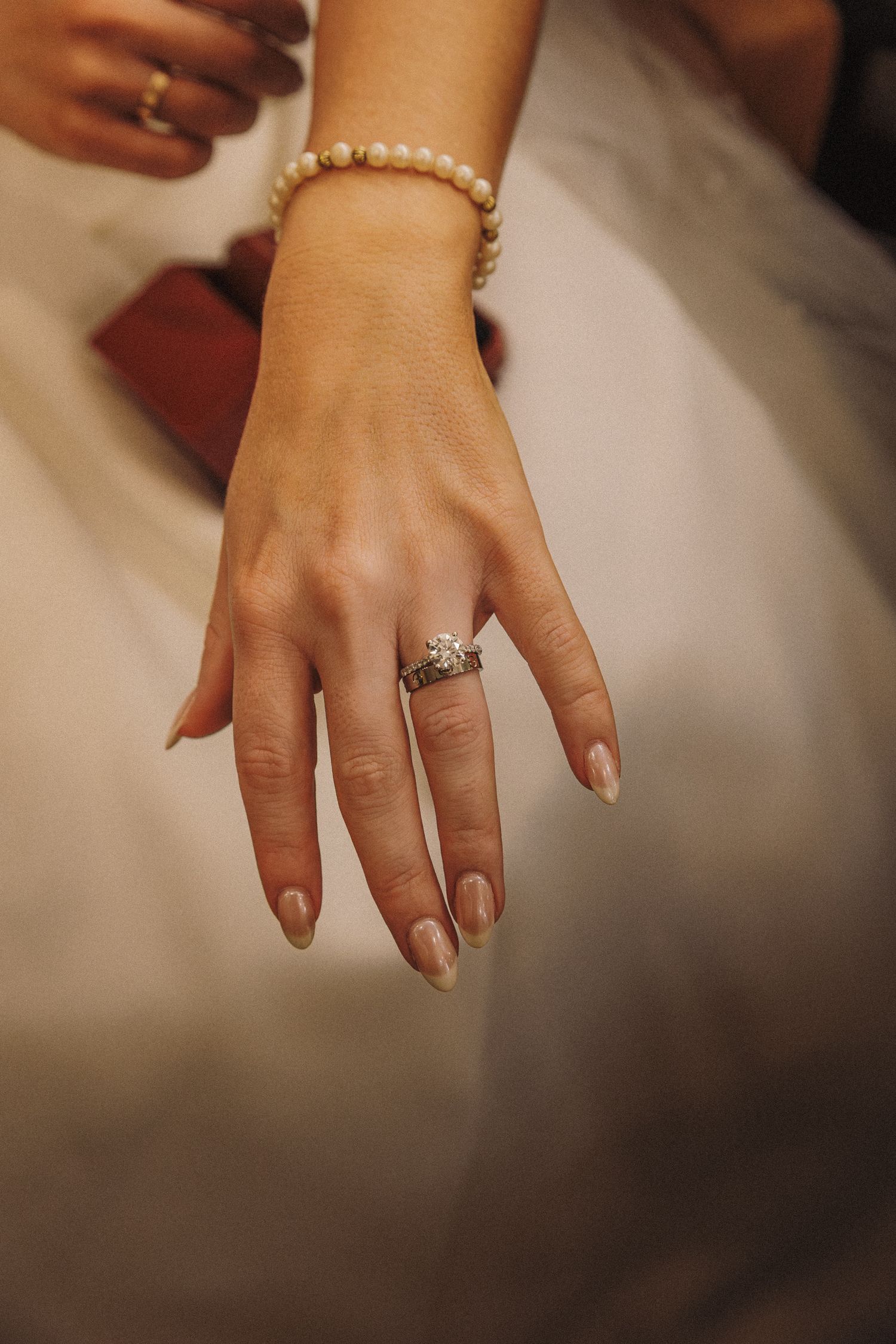 Bride displaying diamond engagement ring and pearl bracelet on her hand in wedding attire.