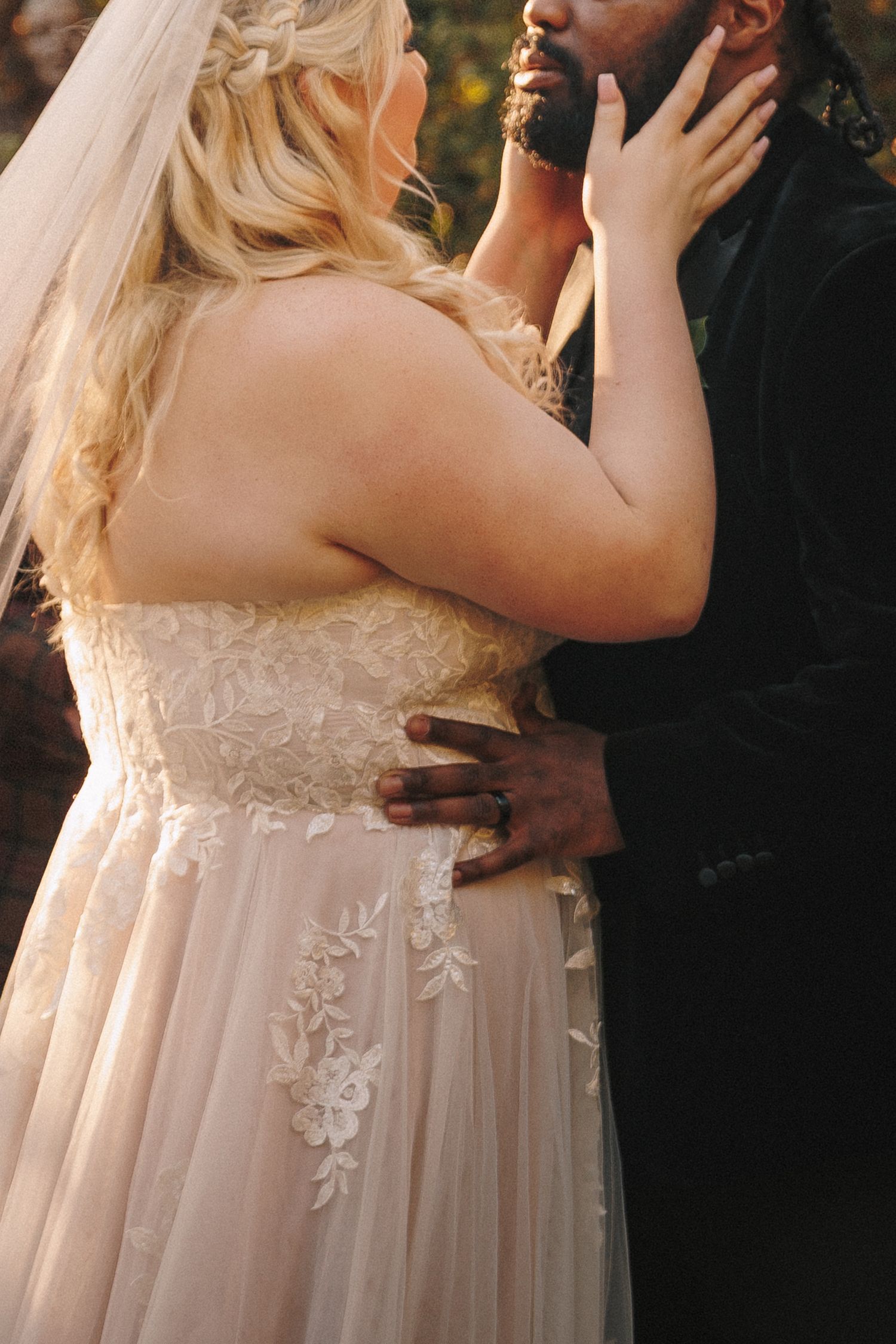 Bride in lace wedding gown and groom in black tuxedo share an intimate embrace at ceremony.