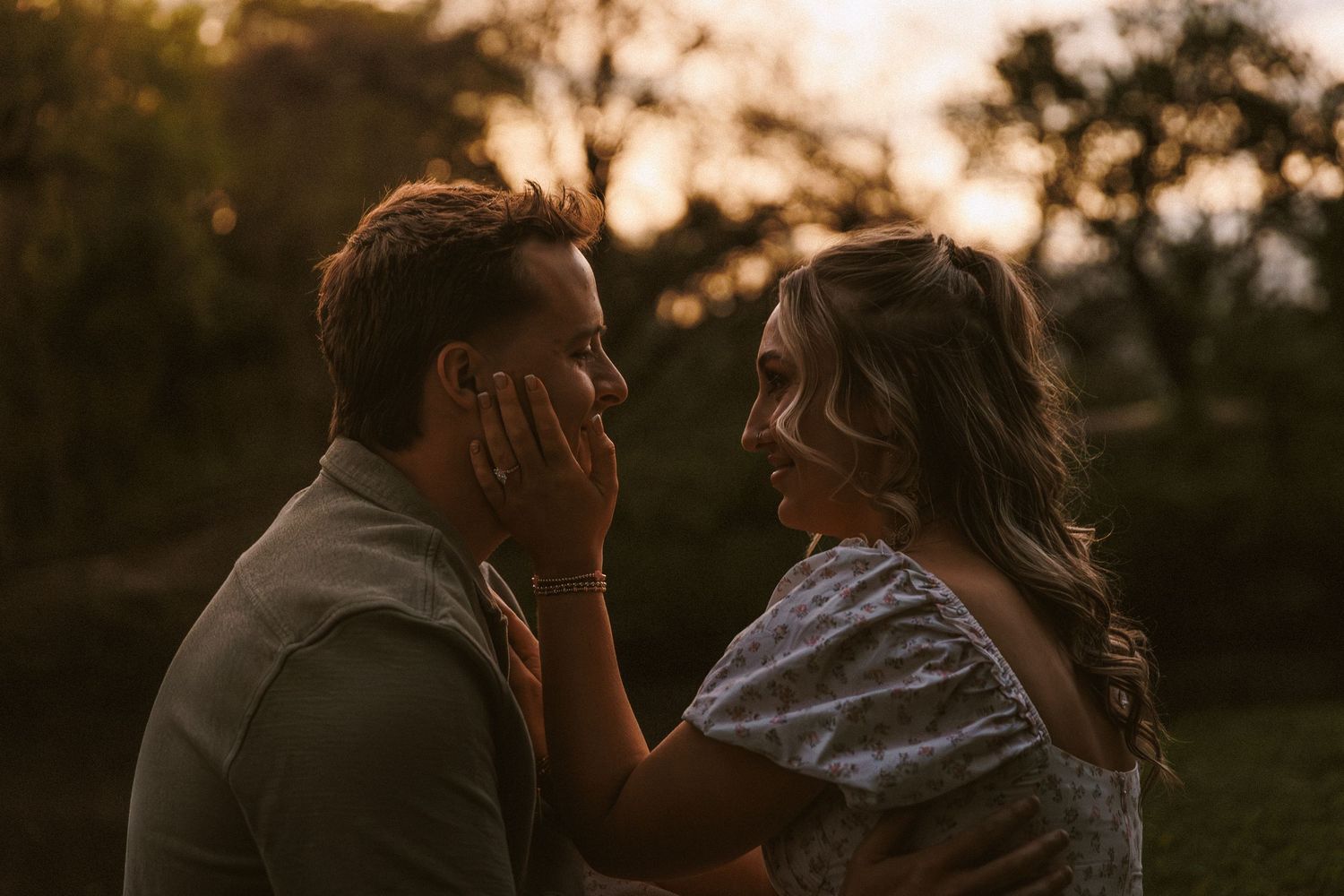 Romantic couple sharing a tender moment at golden hour, woman gently touching mans face outdoors.