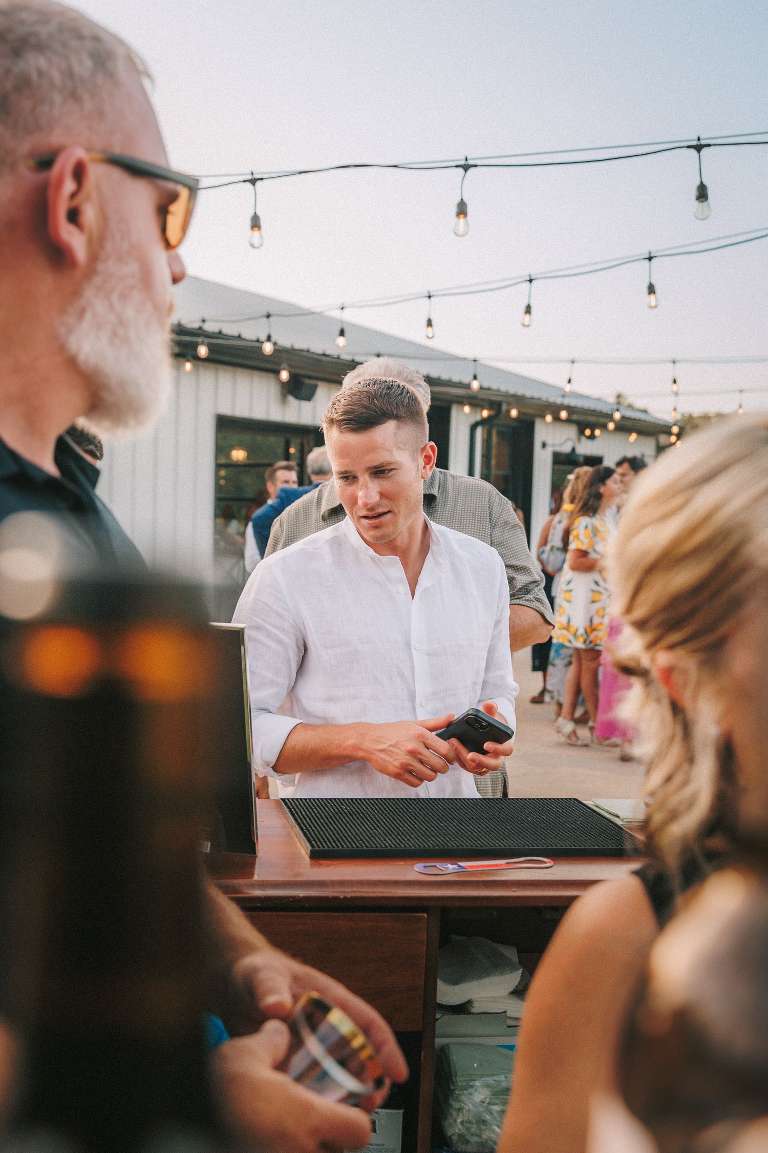 String lights hung above an outdoor bar area at a wedding reception.