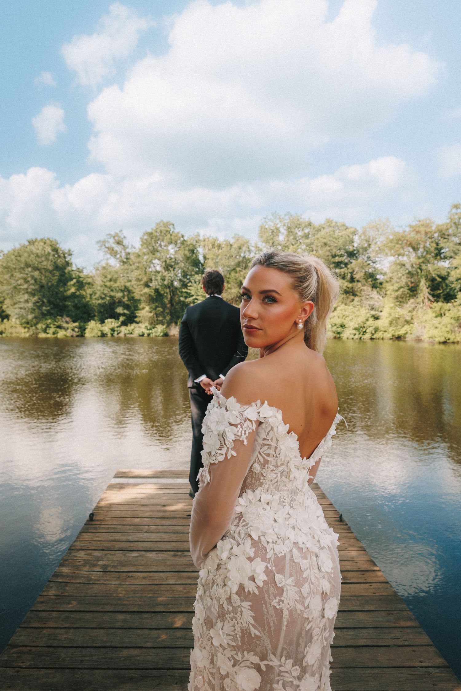 Intimate wedding photo on dock showing detailed lace dress and lakeside backdrop.