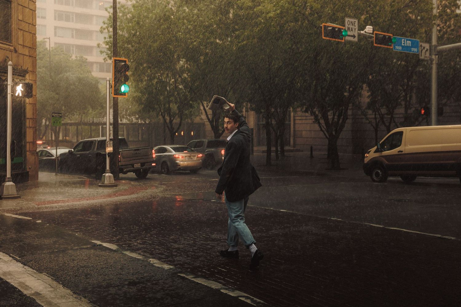 A dark urban street scene at night with heavy rainfall illuminated by streetlights and car headlights.