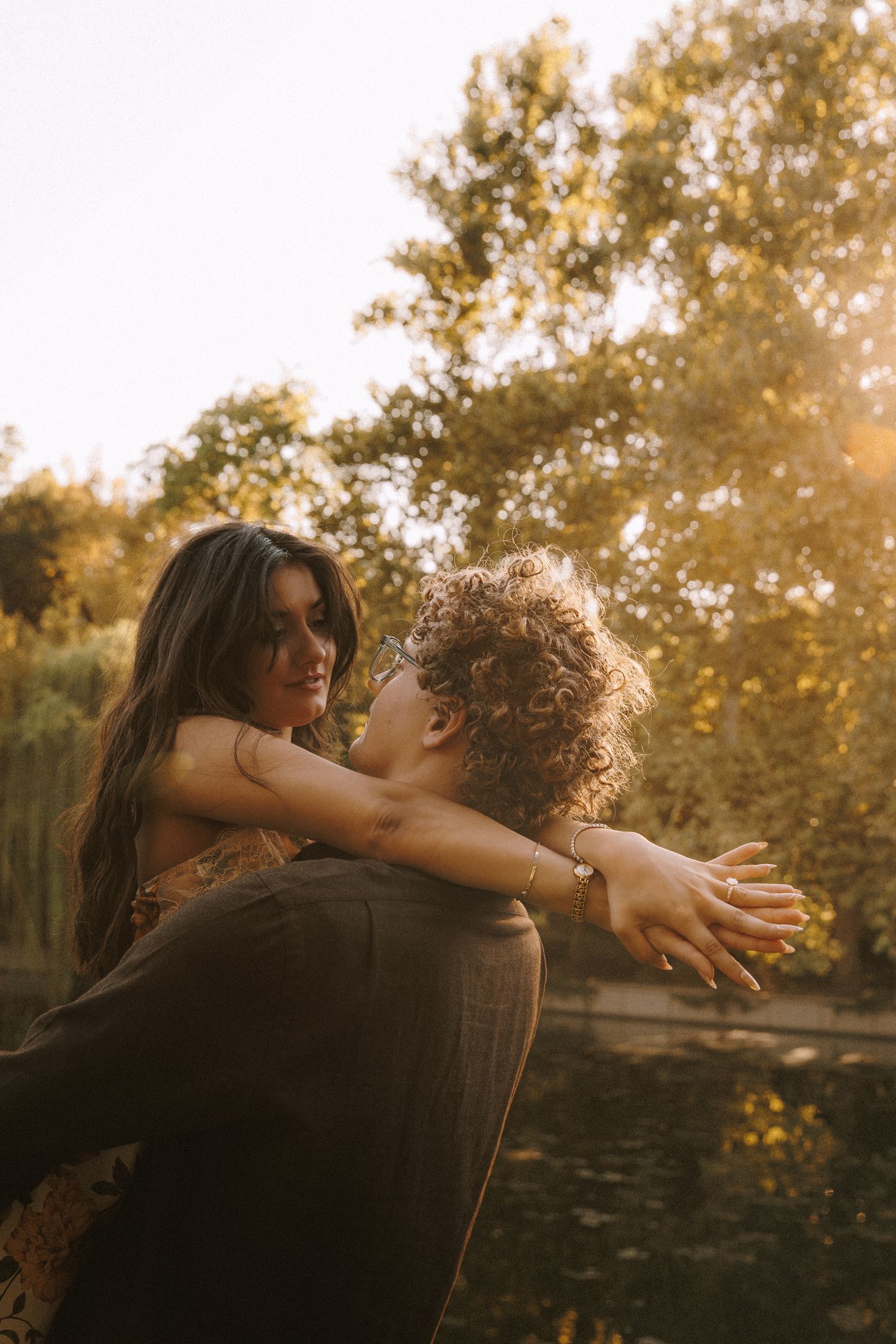 A couple embraces in a warm golden sunset light while surrounded by trees in a romantic outdoor setting.